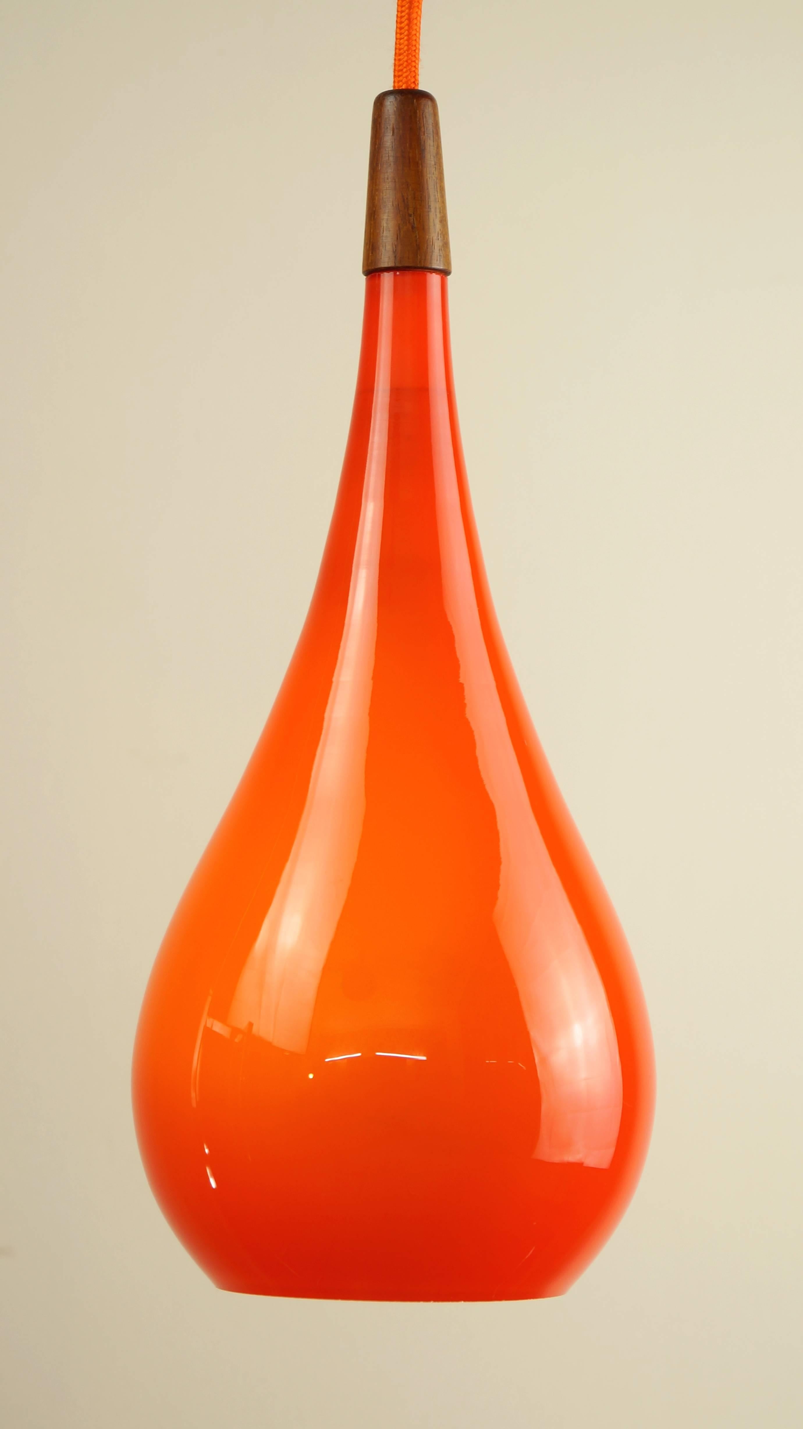 Vintage orange glass and teak pendant light.
Designer: Holmegaard, Denmark,
circa 1960s.

A beautiful handblown 1960s orange glass pendant drop light by Holmegaard, circa 1960s.

Finished with a lovely solid teak final to the top, and