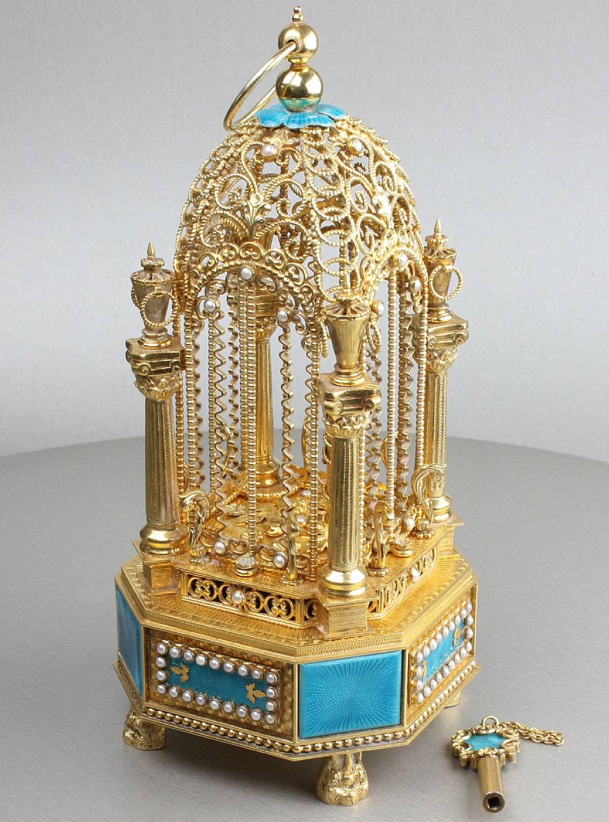 An exquisite vintage rich silver gilt, turquoise enamel and mother-of-pearl mounted miniature singing bird-in-cage and key, by Karl Griesbaum.
 
First half 20th century.
 
925 silver mark.
 
A video is available of the bird singing, please