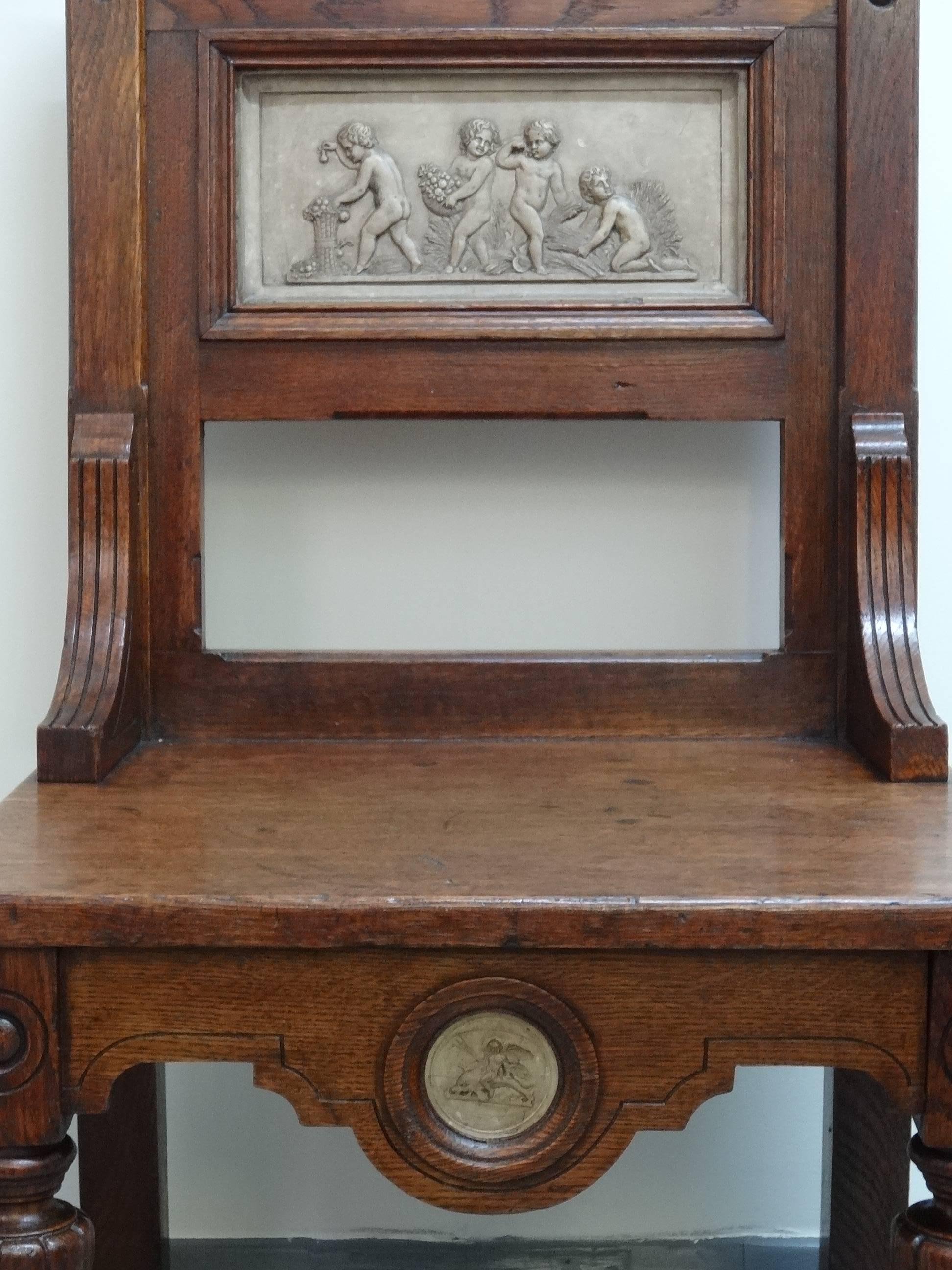 Arts & Crafts late Victorian period oak hall chair; possibly by Gillows of Lancaster or the firm of Marsh Jones & Cribb. Two plaster/earthenware panels; top one of putti/children playing and lower circular one of winged putti with trident