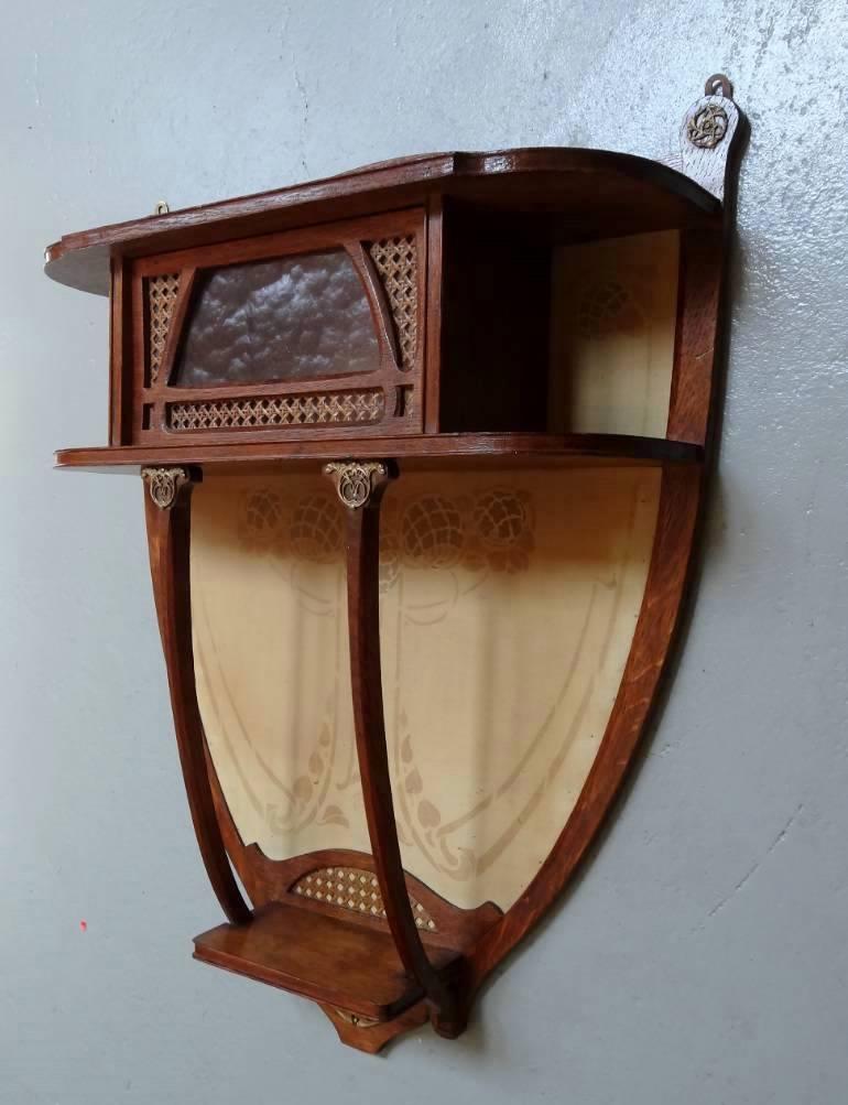 Superb small oak Art Nouveau wall hanging shelved display cabinet with highly decorative gilt metal embellishments and original silk textile backing with, as yet, unidentified monogramme "MG" or "GM" to the silk. 

Mottled