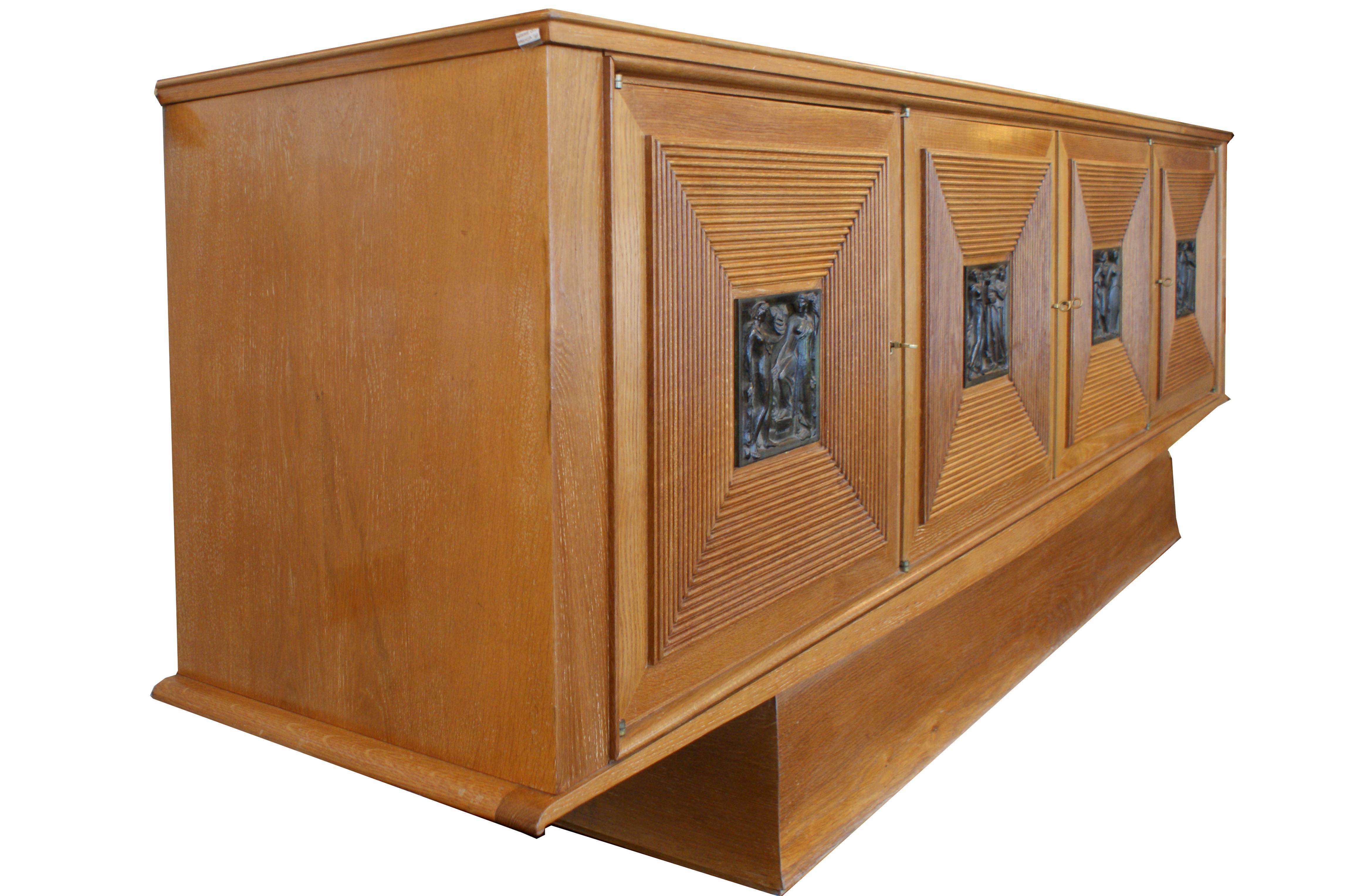 An amazing and publicated four doors cabinet in oak with squared bronze decorations by Maxime Old, France, circa 1940. Signed. Dimensions: cm 241 x 50 x 87.5 H.