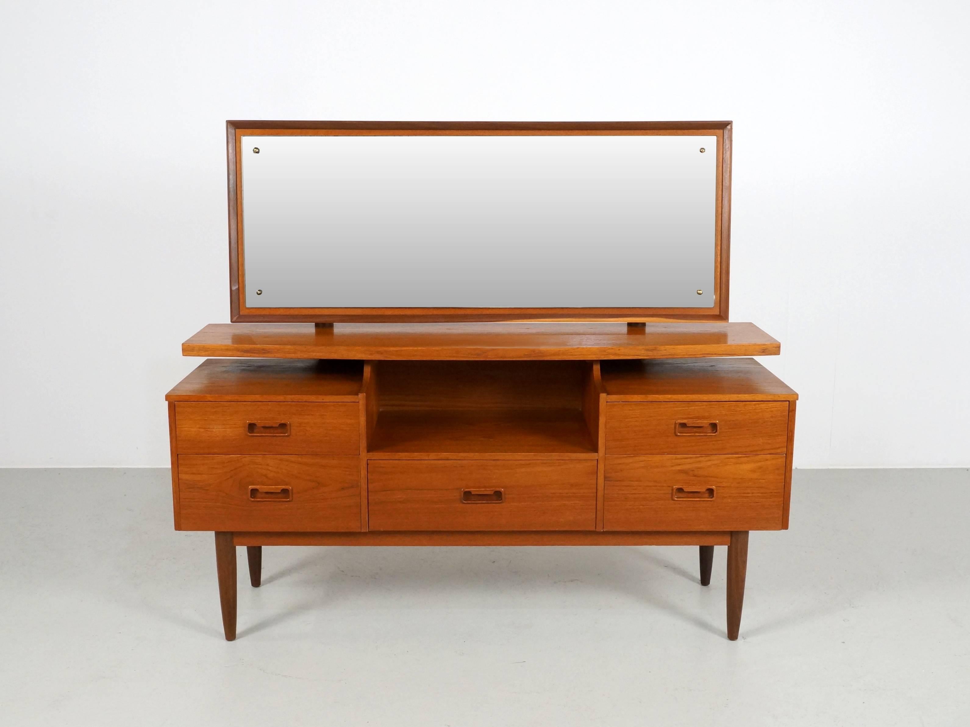 A really useful and attractive vanity or dressing table in teakwood, nicely designed with a wide mirror which stands slightly above the cabinet base part. Attractive Danish modern design with tapered legs and carved inset pulls and a generous amount