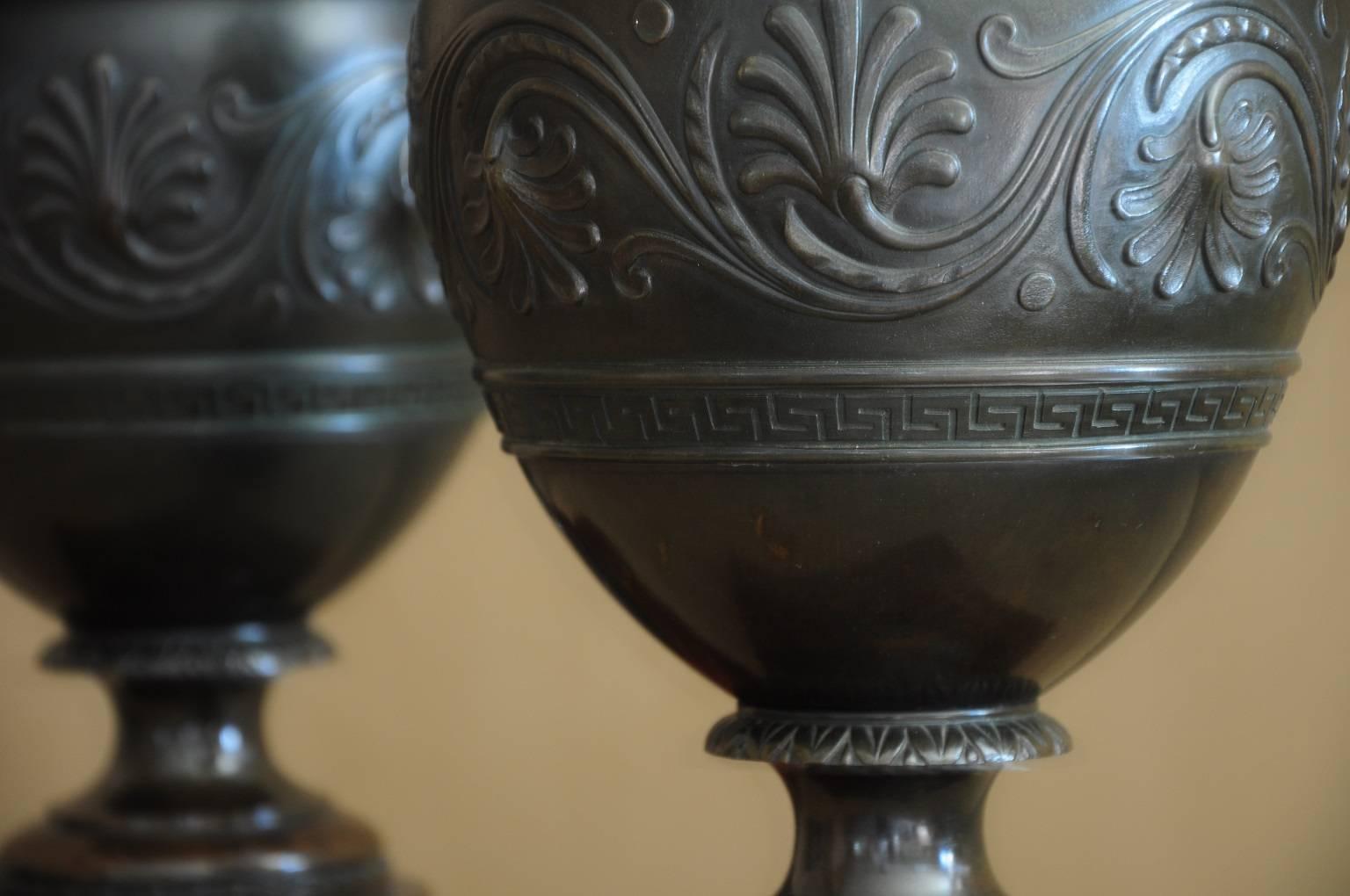 Lovely pair of 19th century bronze urns on a original marble base. The vegetal motives, meanders and lobbed moulding are typical of the Classic revival period. Beautiful detail are the serpents handles which complement the elegant curves.