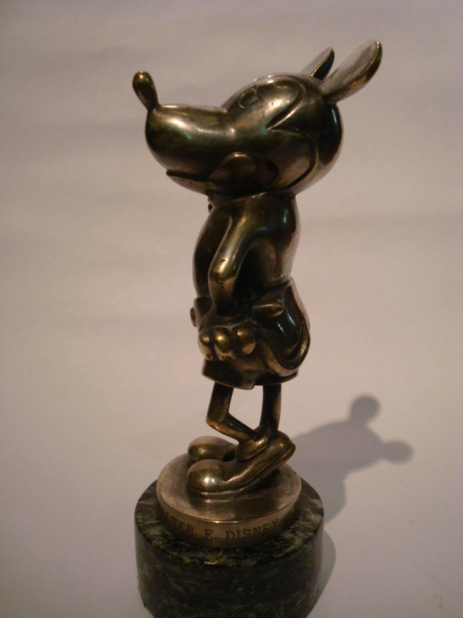 A rare Mickey Mouse car mascot, British, circa 1930, made of bronze Nickel plating, with engraved inscription around the base 'Reproduced By Consent of Walter E. Disney', depicting the film star in jaunty pose, one hand on hip the other giving