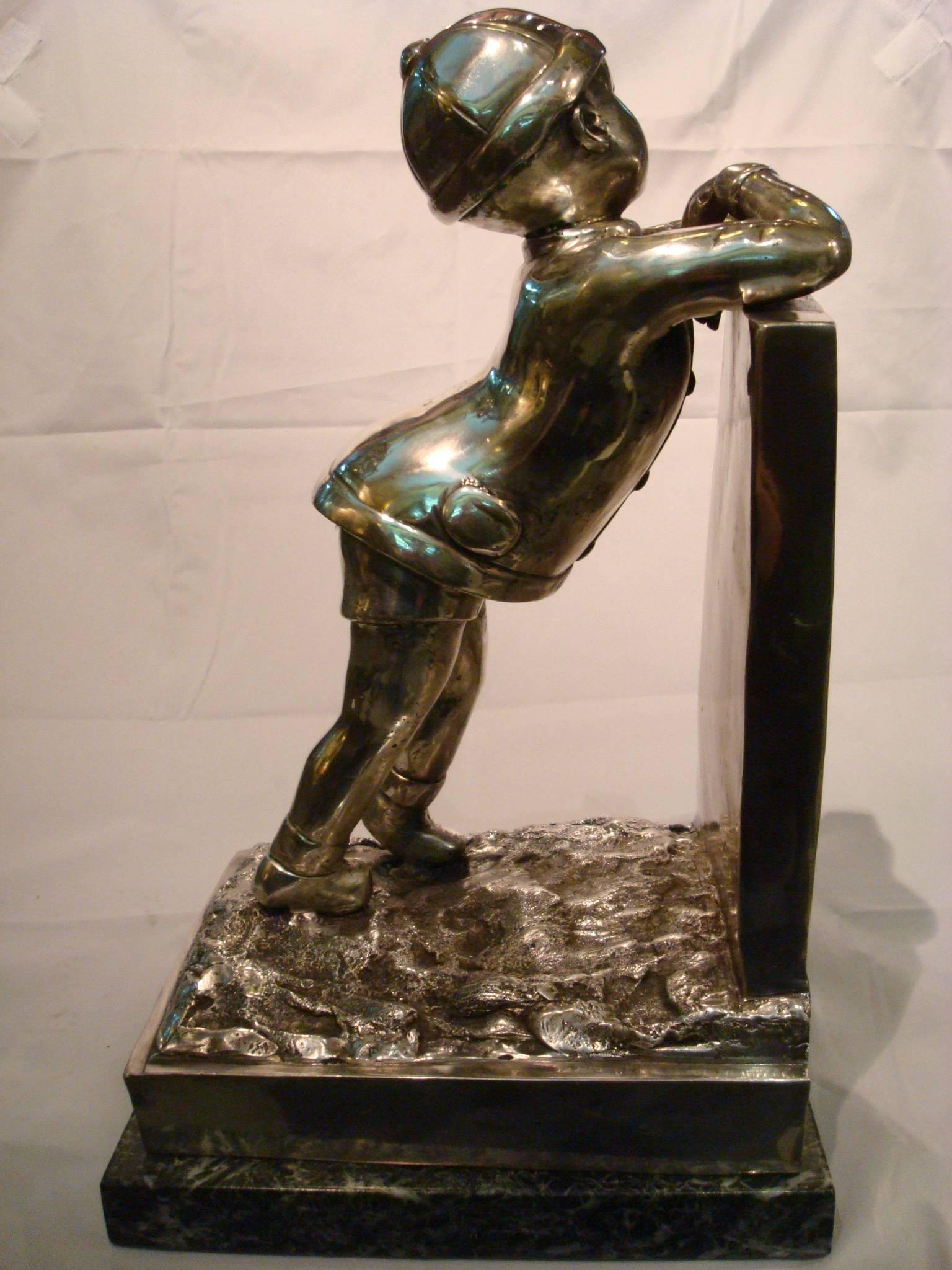 Large Art Deco sculpture of boy looking over the fence. Signed A. Kelety. Silvered bronze-mounted over green marble. Russian Boy with Classic snow hat, same character used by the artist in other figures.