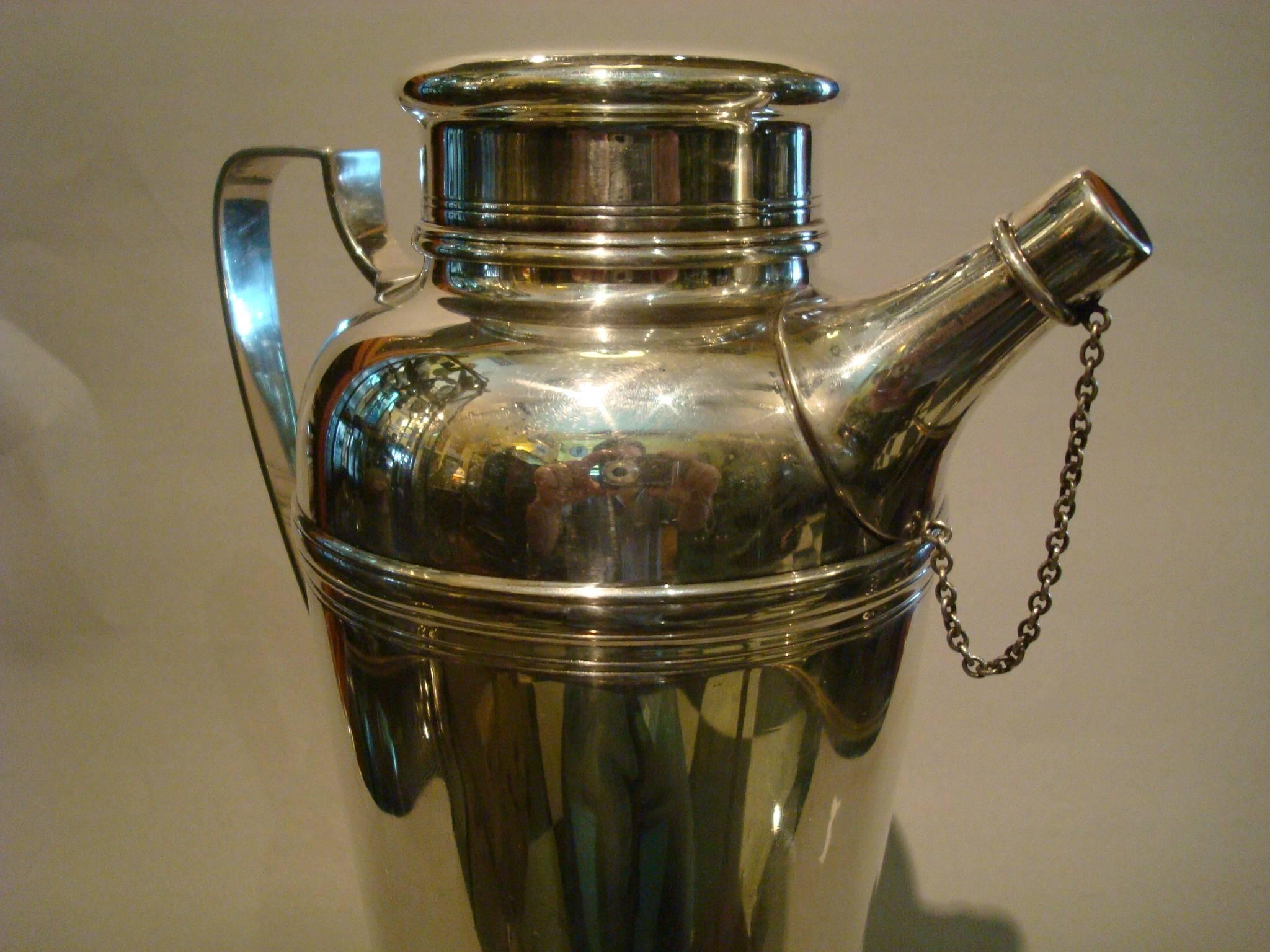 Tiffany Art Deco sterling silver cocktail shaker, circa 1920, Tiffany & Co, New York. The plain tapering body with ribbed upper section and cover, half shield handle, the spout with silver stopper and chain attached. Perfect for any barware