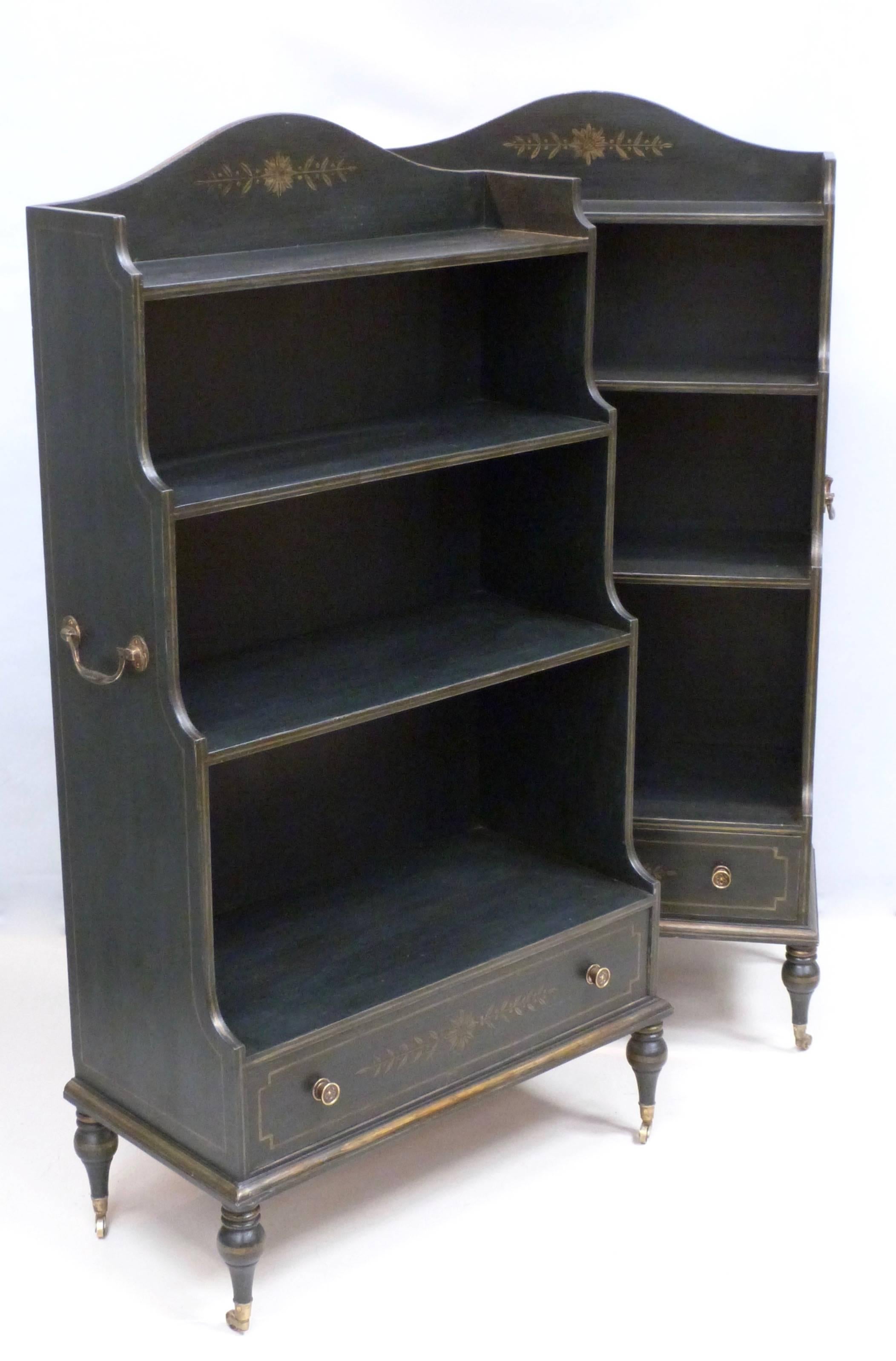 A pair of contemporary ebonized waterfall bookcases in the style of George III, with brass carry handles and brass castors.