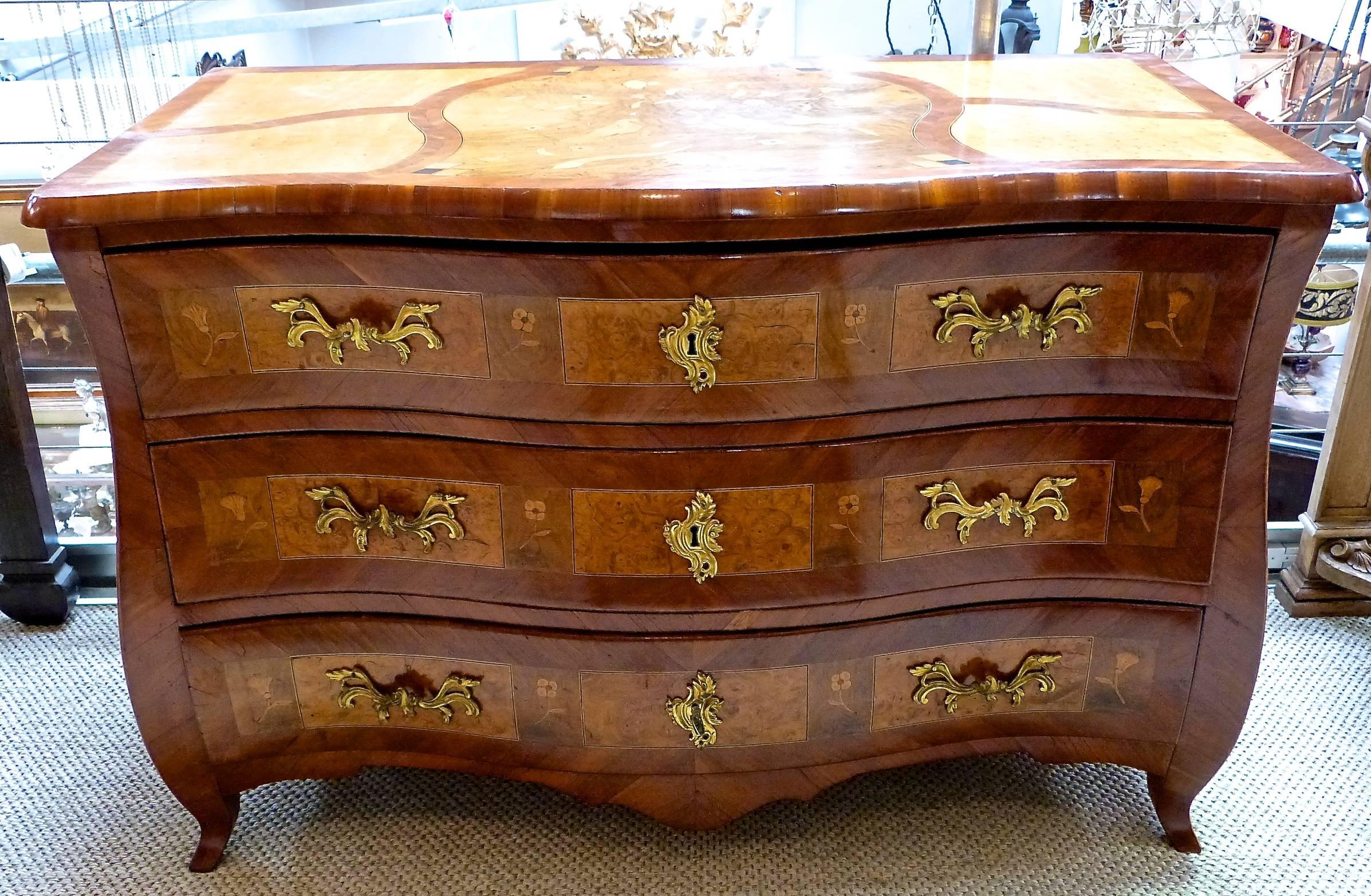 A late 18th century three-drawer bombe commode with gilt metal handles, the top with a panel depicting birds.
