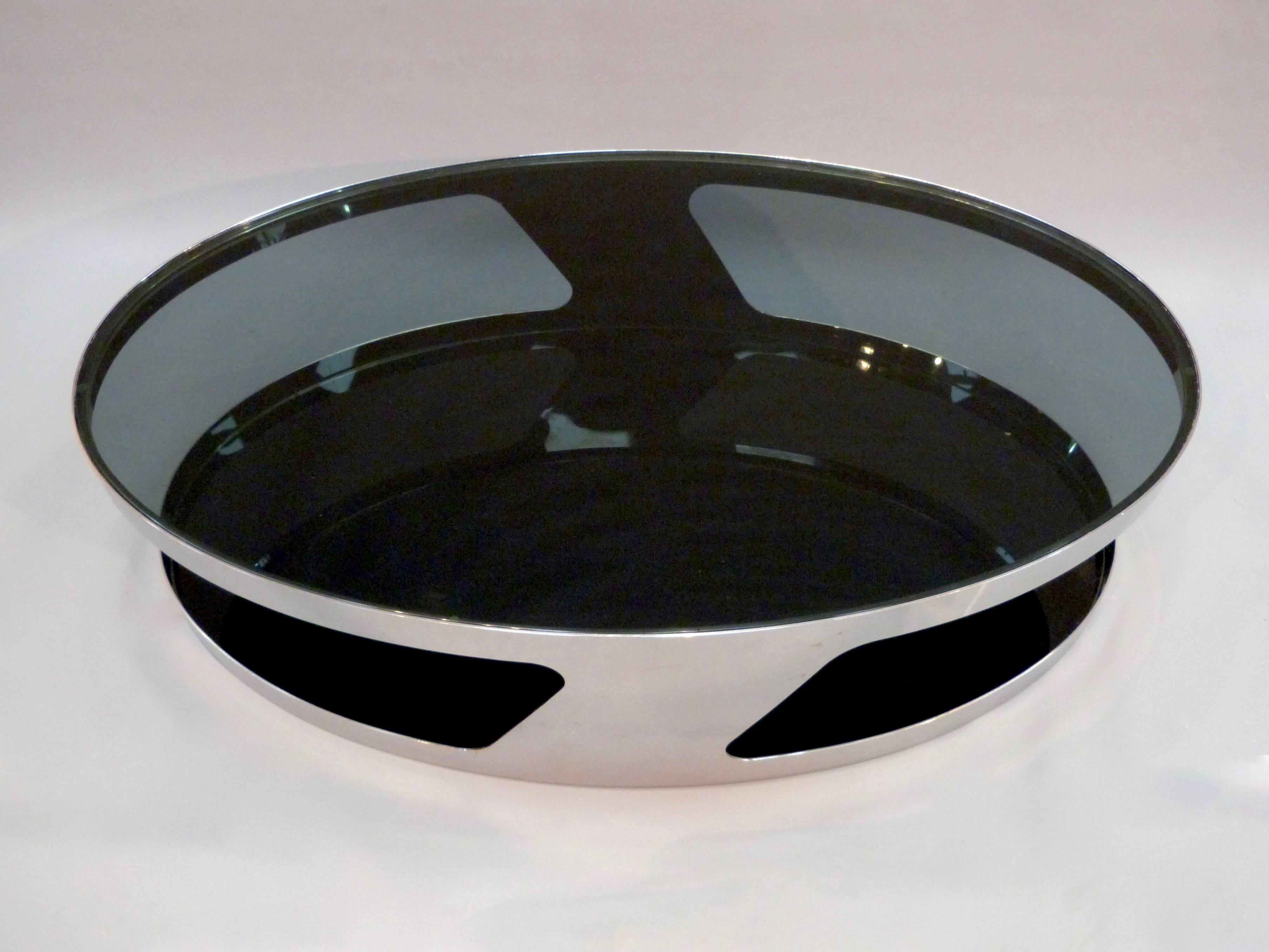 A oval chrome coffee table with smoked and black glass top and shelf.
 