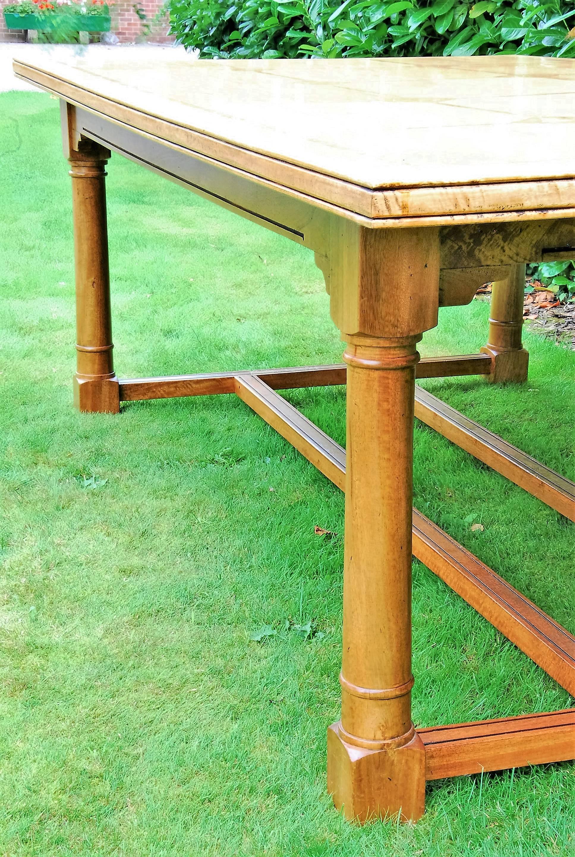 A custom-made turned and worked walnut dining table in the style of John Makepeace. Top inlaid with stone marquetry and supported on gun barrel turned legs united by end and centre stretchers.