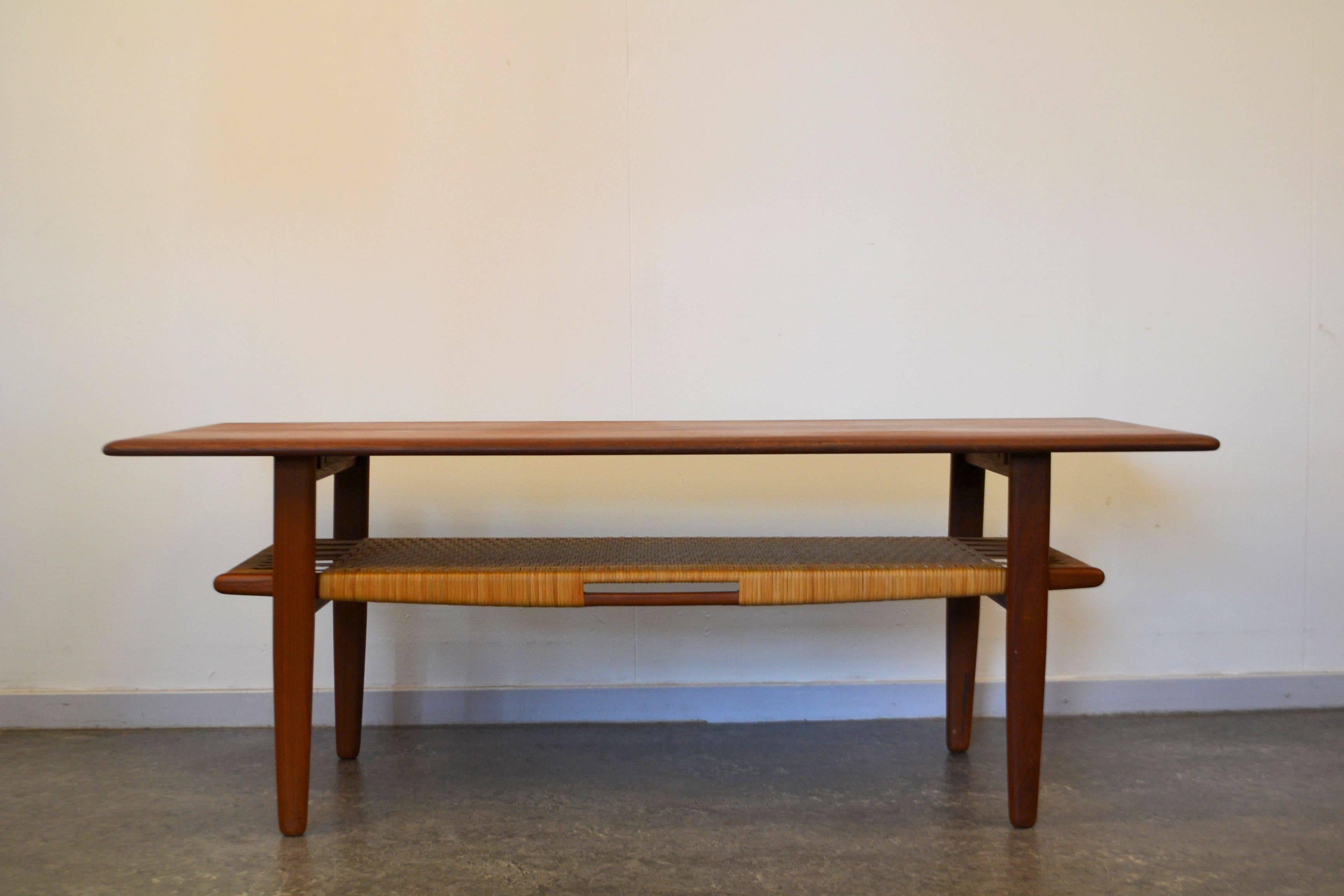 Gorgeous teak Danish modern coffee table designed by Kurt Østervig for Danish manufacturer Jason Møbler. The table features beautiful rounded tabletop corners and a rattan storage shelf for magazines and newspapers and such.