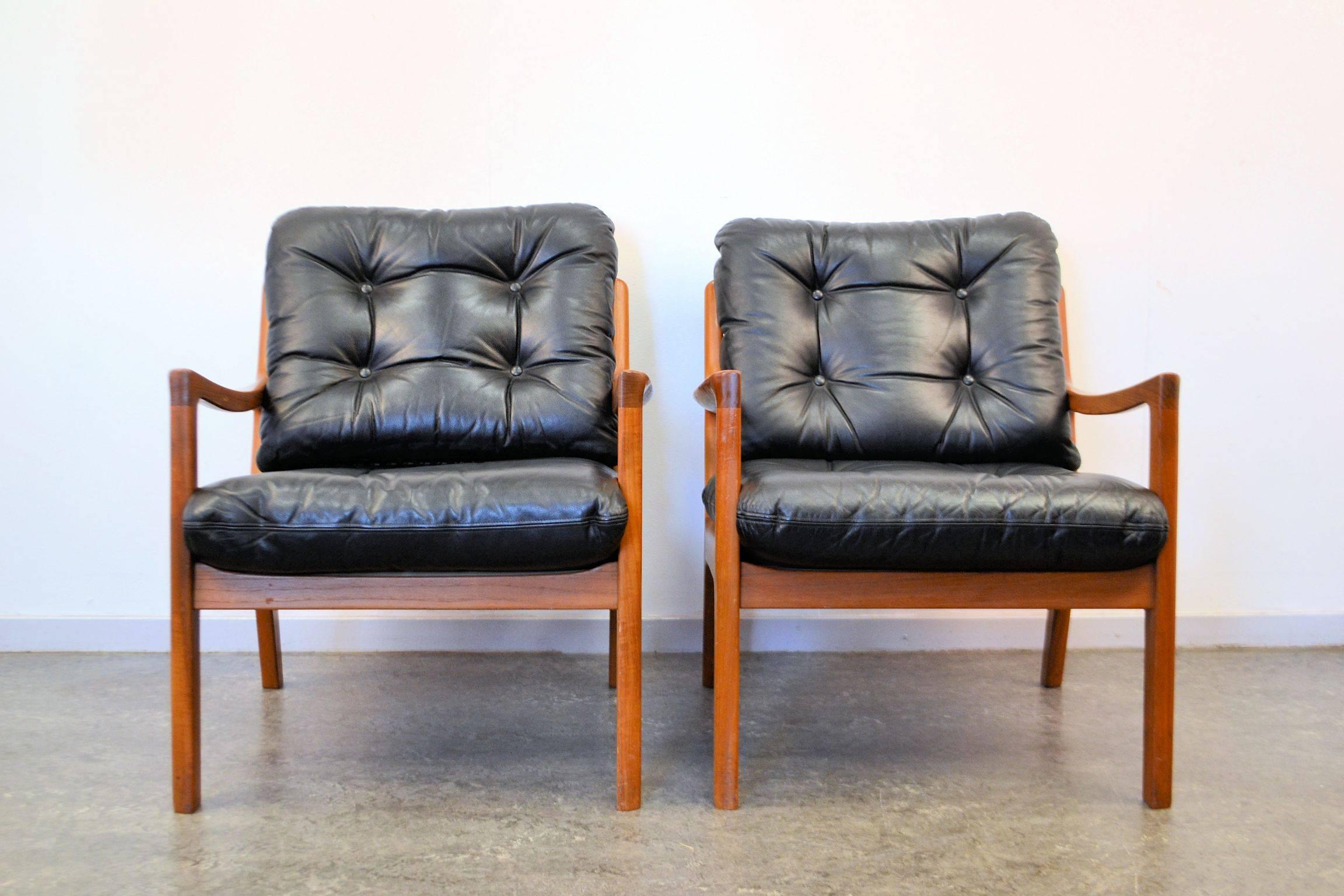 Set of two Danish modern easy chairs designed by Ole Wanscher for Danish manufacturer France & Son. These super comfortable chairs feature solid teak frames and padded black leather upholstery on loose back and seat cushions. Super stylish in both
