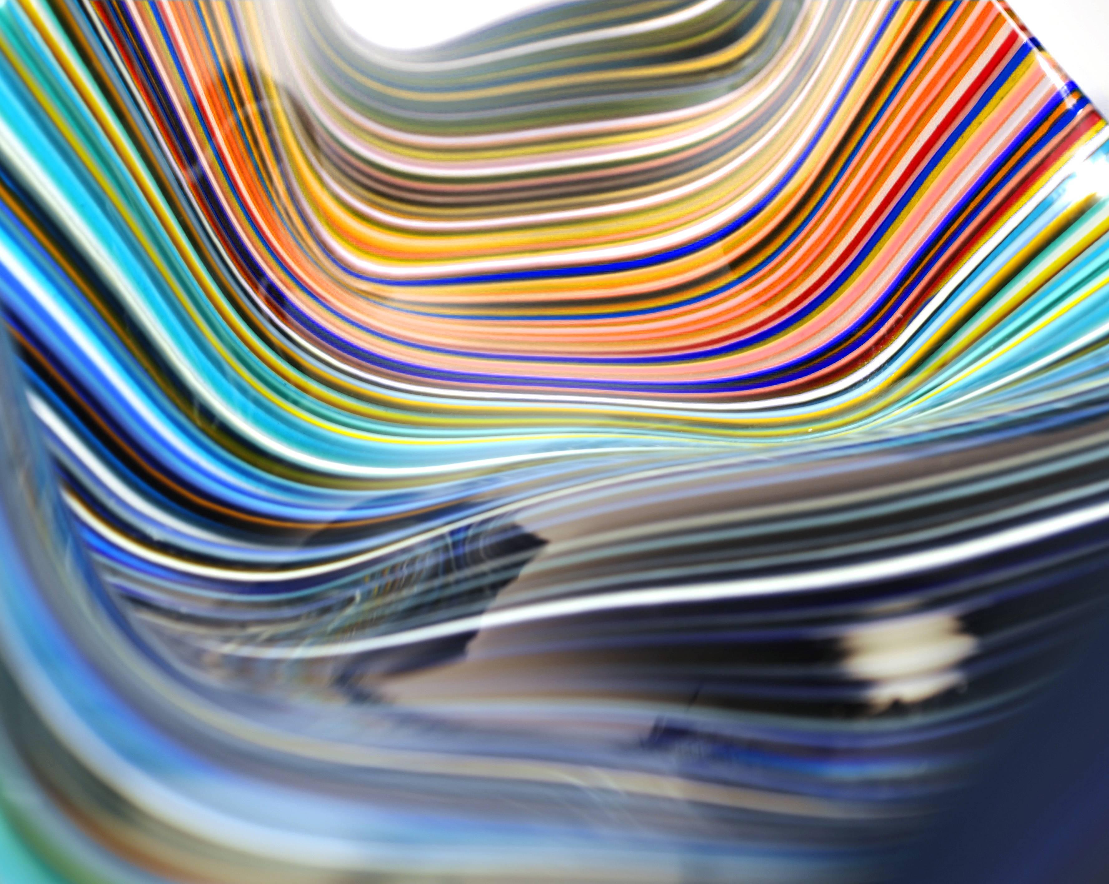 Questo centrotavola lineare e lungo, disegnato da Orfeo Quagliata, si distingue per la sua forma curvilinea e la gamma di colori, e trasmette un'atmosfera che attrae. Un oggetto in vetro fuso e termoformato creato con tecniche esclusive