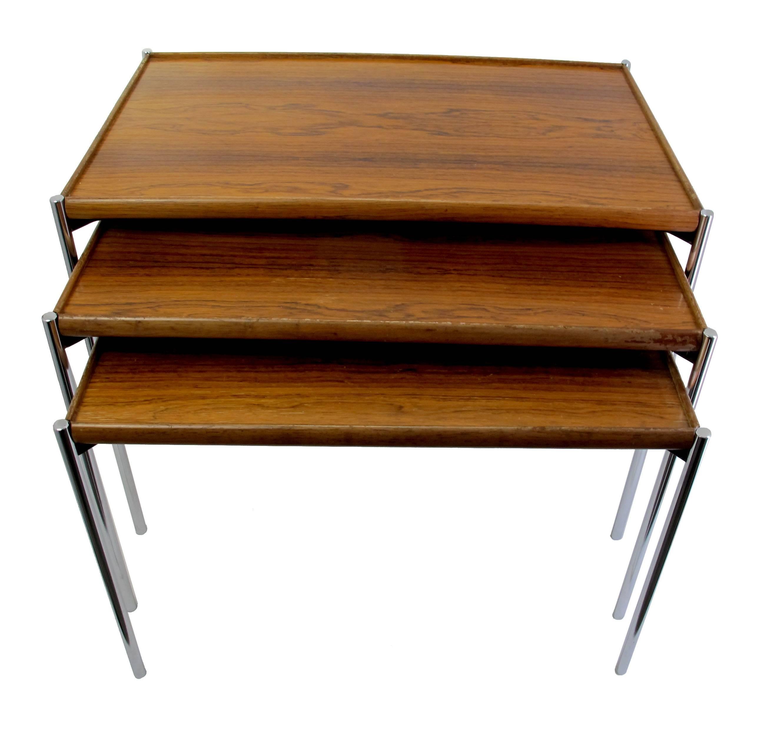 This set of three reversible, model 125 teak nesting tables was designed during the 1960s, and manufactured in Germany by Lämmle & Co. Each table features stainless steel legs and a teak table top which can also be used on the white reverse side.