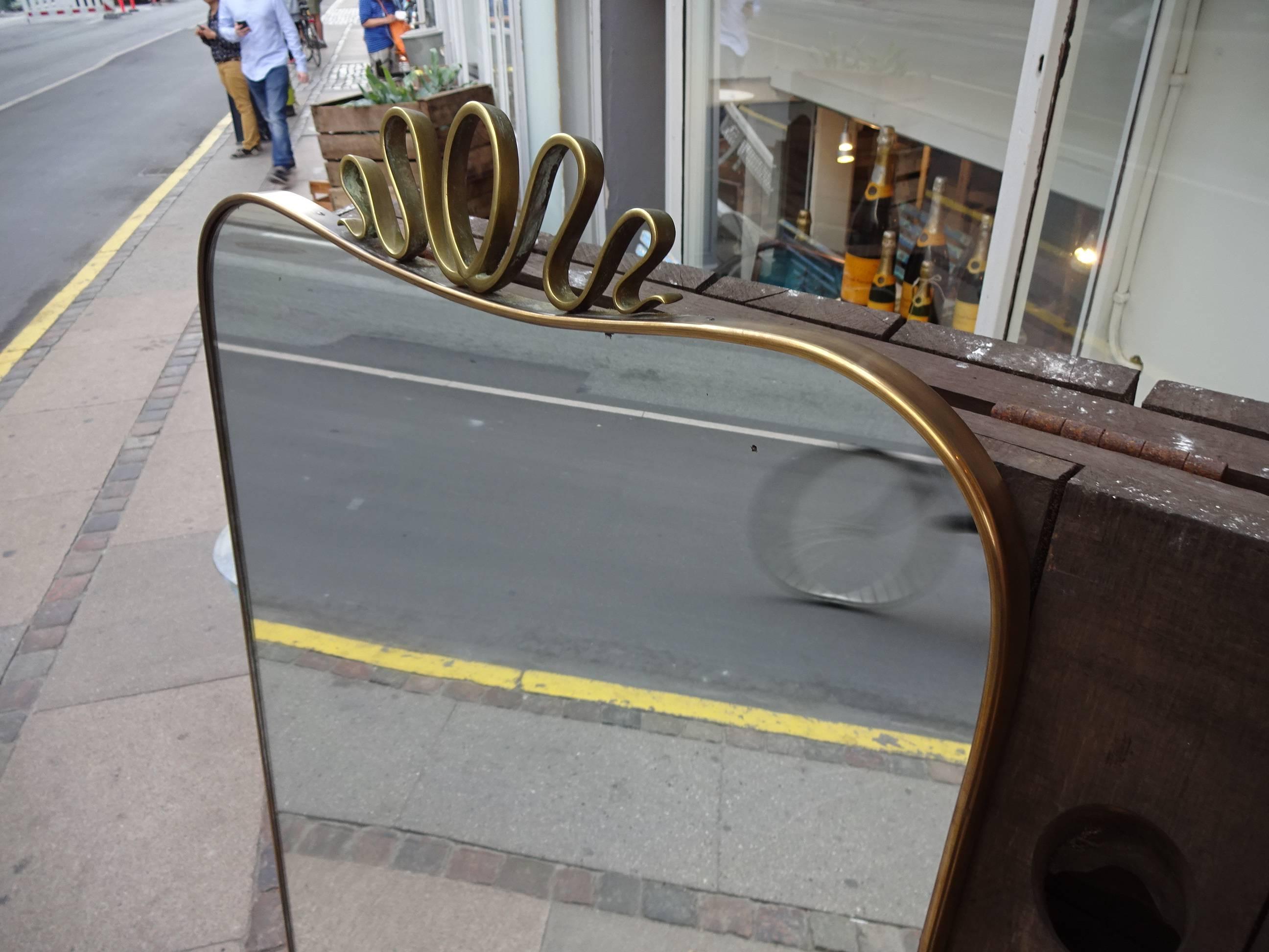 Large elongated Italian brass mirror from the 1950s and with a style akin to Gio Ponti mirrors. Original mirrored glass, and the brass frame has lovely patina. The stunning ornamental work at the top makes this item a unique piece indeed.