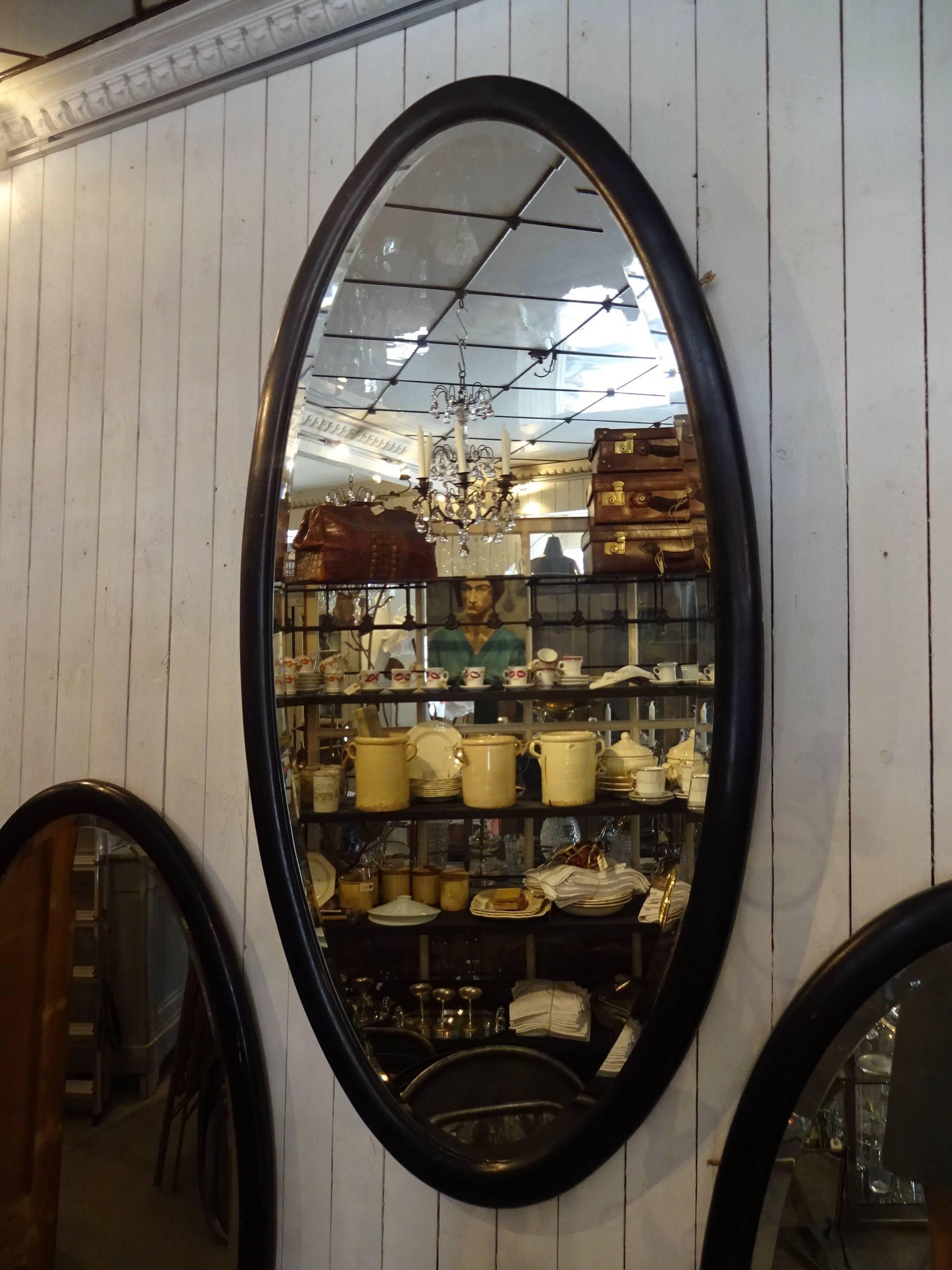Antique oval French mirror from the early 20th century. The mirror has a stunning wide black painted wooden frame, and beautifully original face-stained glass.
At the moment we have three identical mirrors in stock. 


