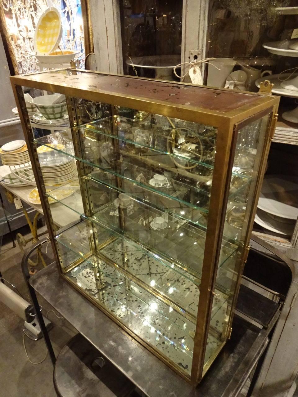 Beautifully patinated old French display cabinet in brass with glass doors at each end. The cabinet has the original mounted wall brackets and three glass shelves. The doors can be shut but not locked.

Measures: H 80 x W 70 x D 20.5 cm.