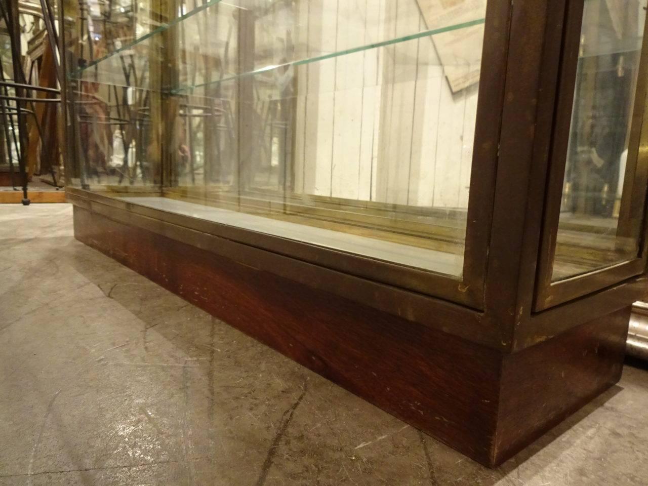 Elegant and narrow midcentury French brass display cabinet from the 1950s, originally used in a boutique. Both ends of the display have doors to access the three glass shelves. Slim and elegantly raised from the floor with a wooden base. Super