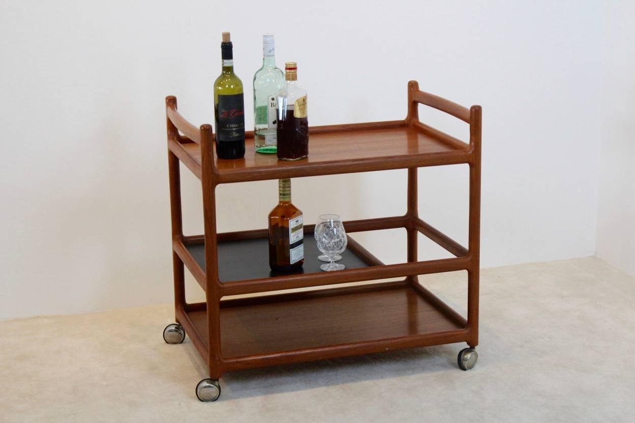 Magnificent teak trolley designed by Johannes Andersen. Produced by CFC Silkeborg Møbelfabrik in Denmark. This bar and serving cart is made from solid teak and one black laminate tray, riding on fully working chrome casters. Excellent and original