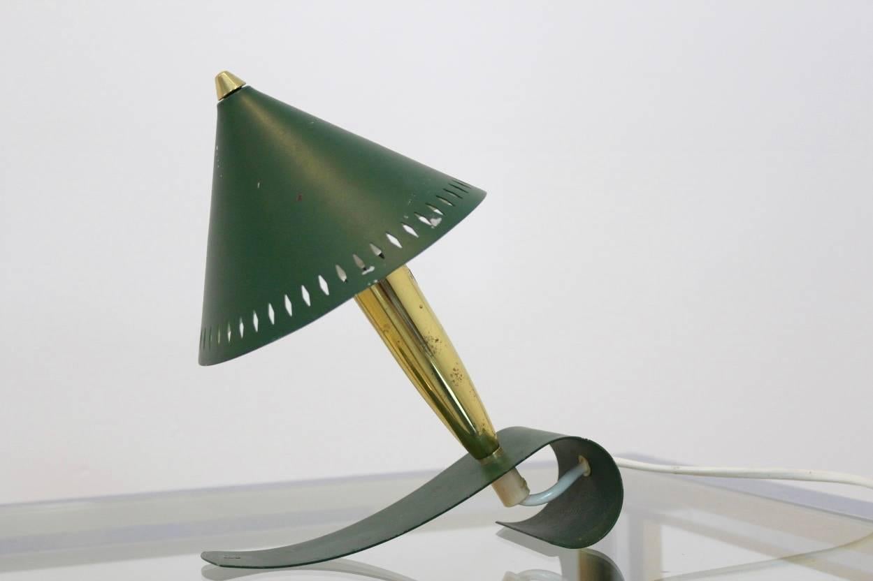 Beautiful Swedish Pinocchio table lamp designed in the 1950s. Also possible to use as a wall lamp! Adjustable green metal shade with a brass foot resting on a green lacquered metal wave. Decorated with a characteristic die cut pattern around the