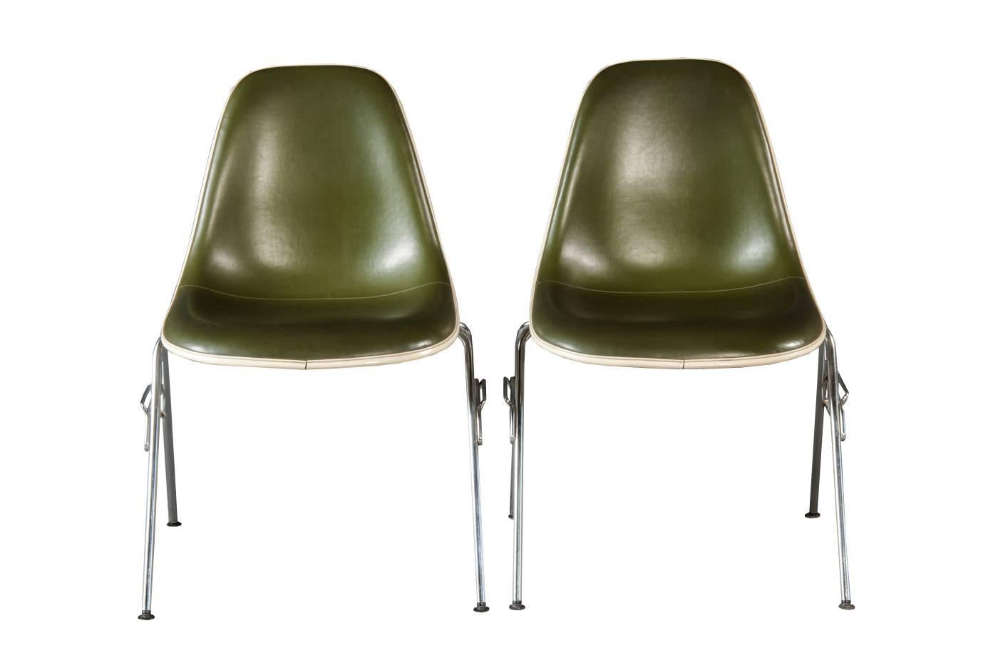 Model DSS chair designed in 1955 by Charles and Ray Eames and produced by Vitra for Herman Miller. 

The chairs feature a cream-colored fiberglass shells on a stacking base with linking element. The chairs are upholstered in original dark green