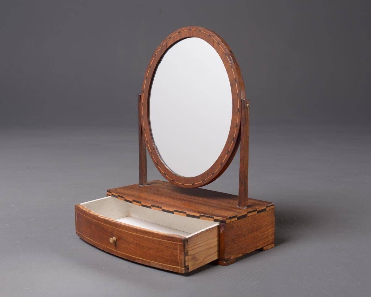 Rare small table mirror which is completely veneered and has graphic intarsia. Neneath the oval mirror there is a small drawer.
Material: Wood, veneered, mirror
Measurements: W.32.5 x D.17 x H.43 cm
Condition: The back cover is partly defect