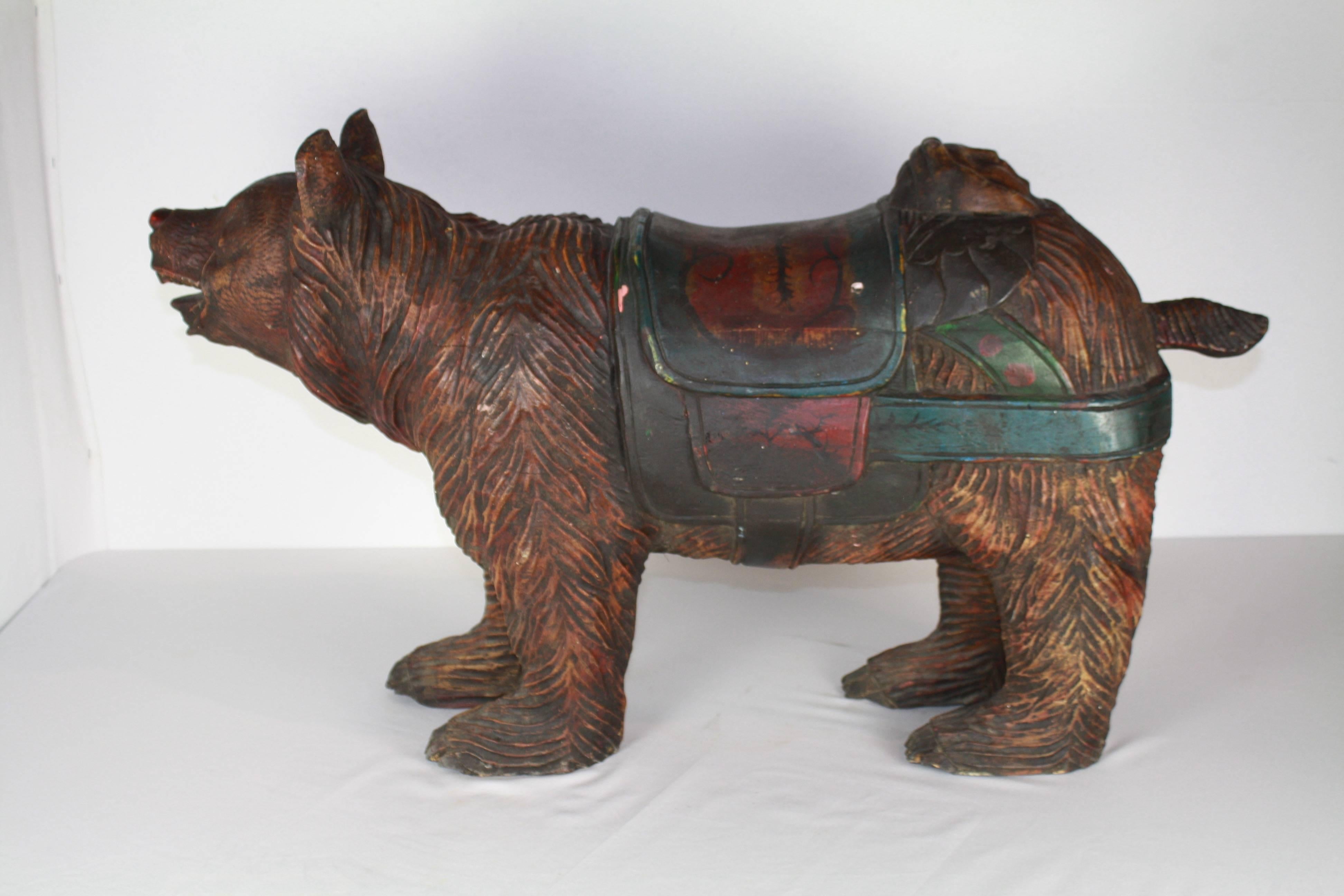 In the style of a late 19th-early 20th century carousel animal, this whimsical bear does not have the pole hole or bracket holes in the feet that would have designated it a carousel animal. A lovely green and red painted saddle adorned with a cherub