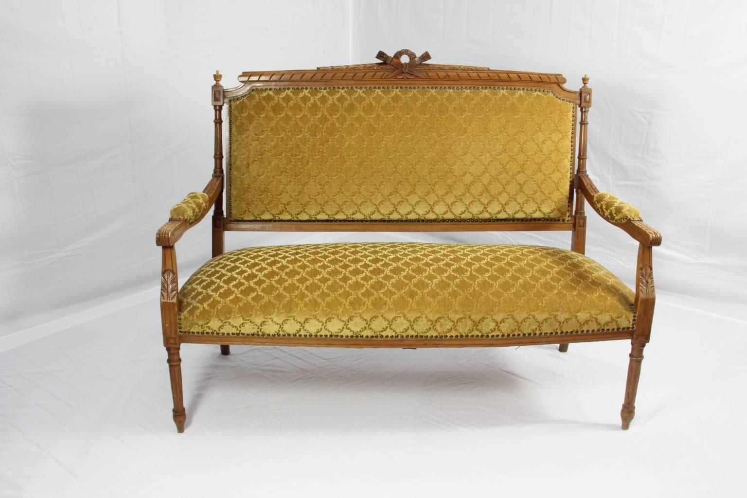 French settee of walnut with golden pressed velvet and brass tacking. The crest rail of this piece features a spiral carving giving the look of a rope tied in a bow in the center, flanked on both sides by acorn finials. Chip carvings up the legs and
