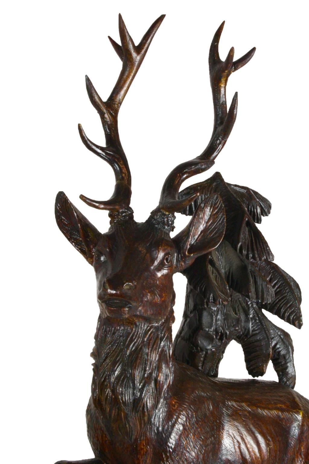 This beautiful example of Black Forest carving, displays the outstanding talent of a master woodworker. Features a red stag atop flora and a tree backdrop. The clock has white porcelain number plates with blue numbers and a French movement, with