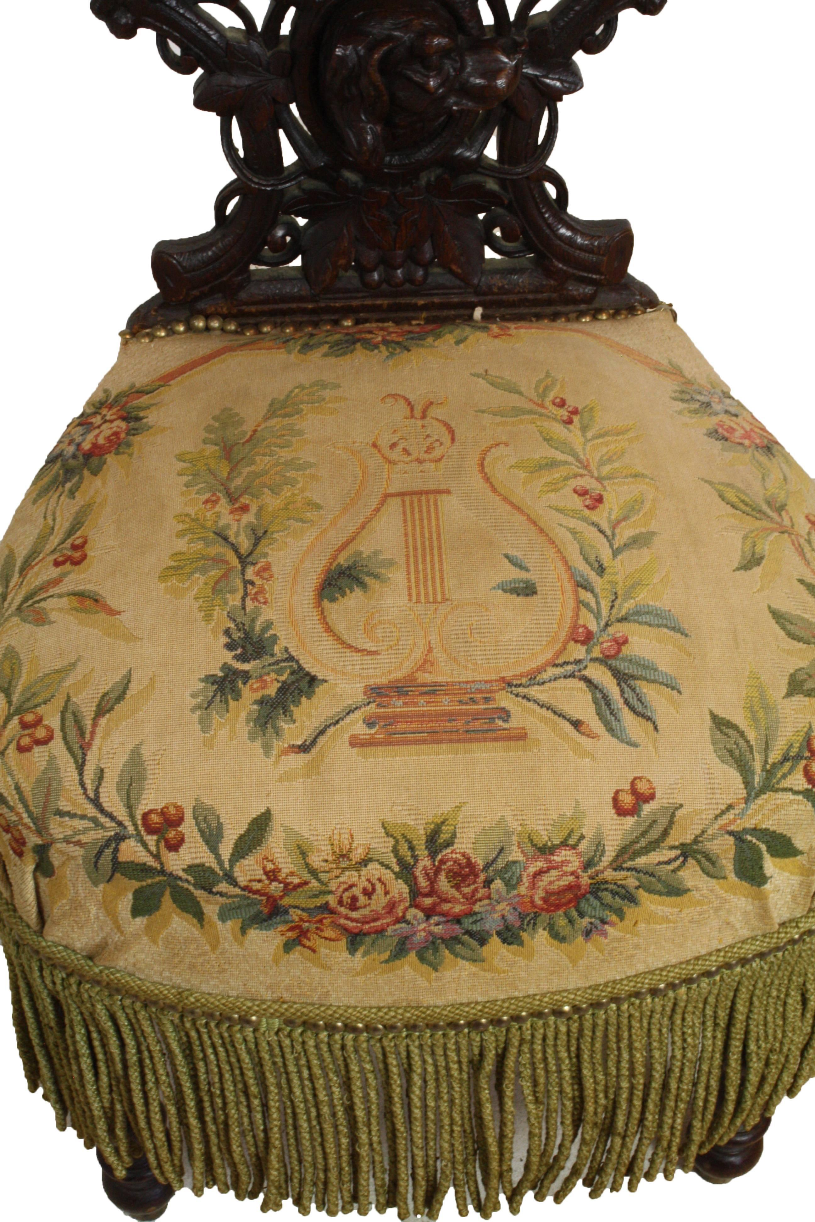 This French smoking chair features a storage area under the back armrest. The musical themed fabric with surrounding tassels gives this intricately carved chair a Haute Boheme (High Bohemian) feel.