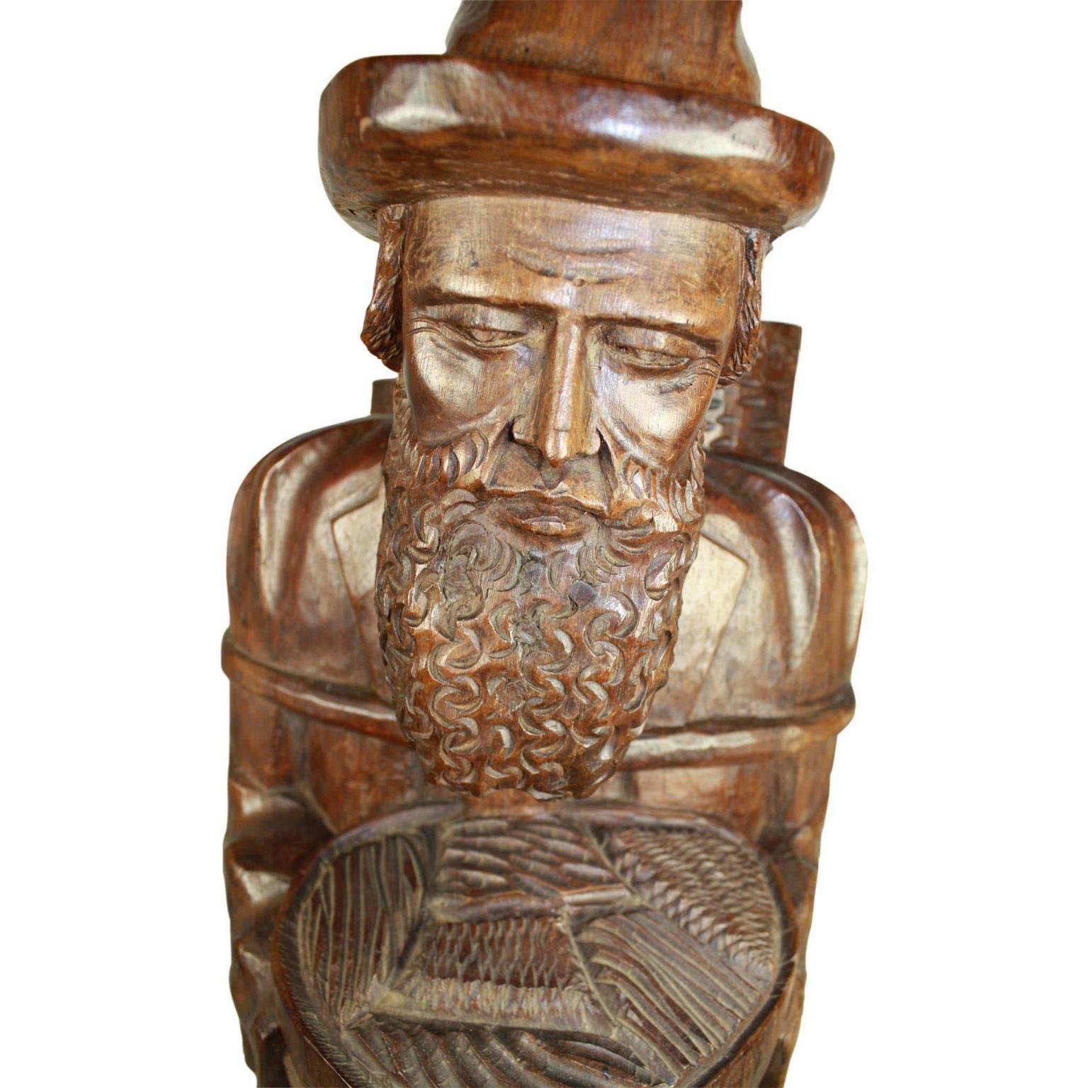 An elderly, bearded, Asian man carries a bowl of food, possibly noodles, with two mats tied to his back. Carved from a substantial piece of teak, this somber carving stands at almost 3 and a half feet tall.