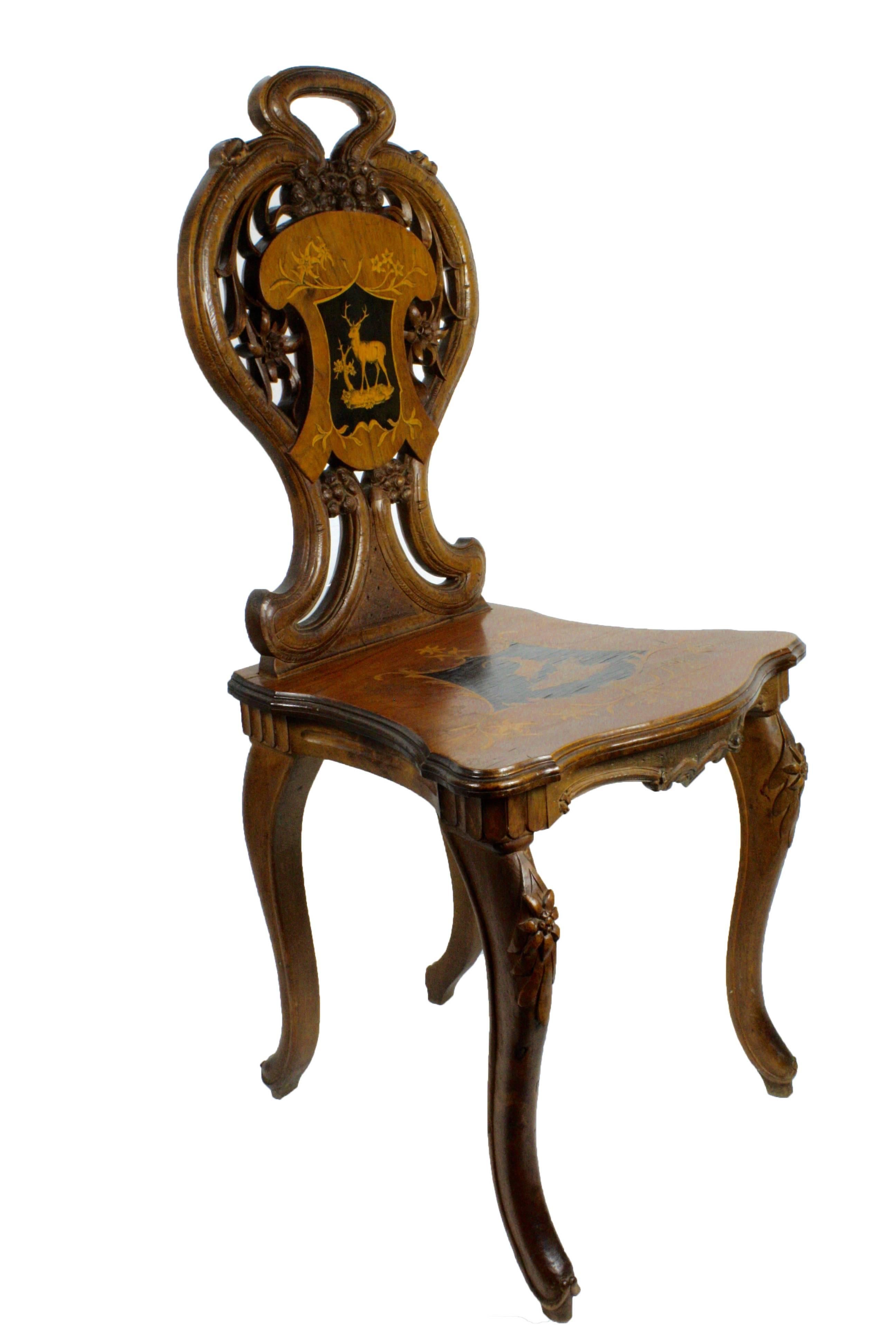 A carved Swiss walnut chair featuring inlaid ibex and stag with delicate edelweiss and floral carvings.