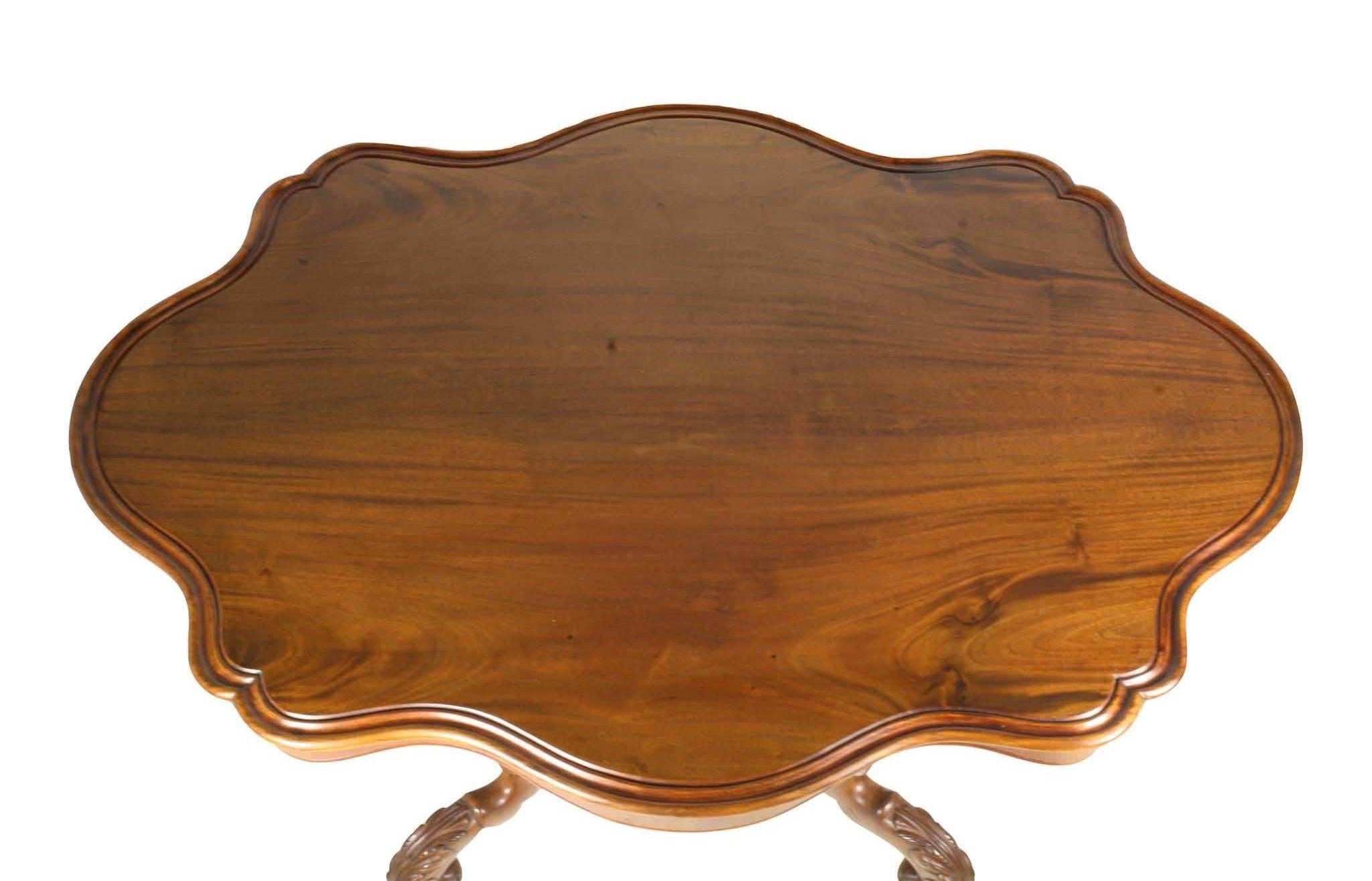 Fine scalloped edging creates the lines of this Dutch occasional table. A quartrefoil base with upper and lower finials is supported by scrolled feet on castors. The mirrored 3/4 inch tabletop is cut of solid mahogany, unlike the many veneered