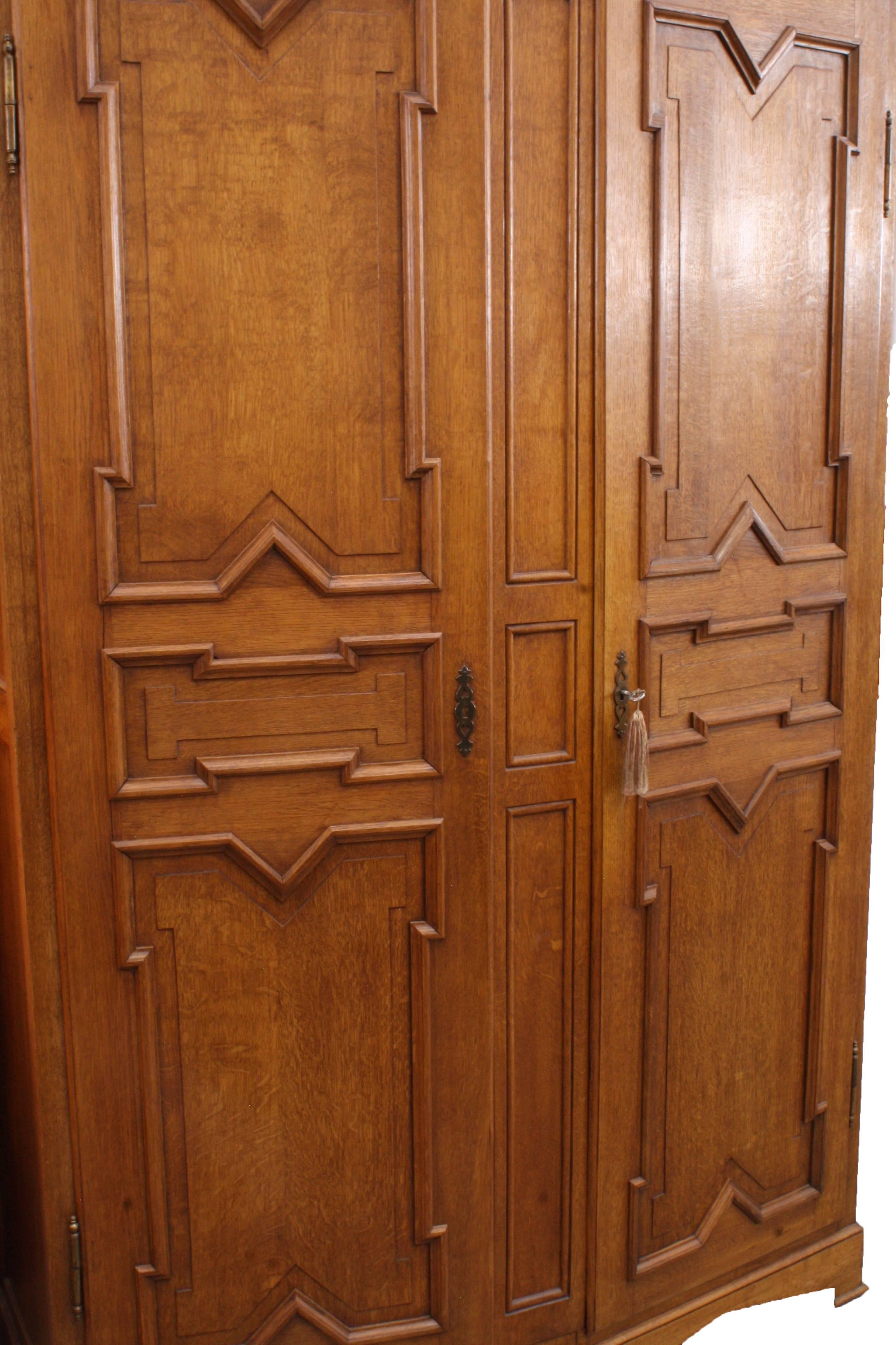 The quarter sawn oak of this simplistic Neo Gothic style armoire, was meticulously picked to match the unique patterns in the wood grain.  Two heavy doors open to reveal dressing mirrors on the inside of both doors and the piece has plenty of rods
