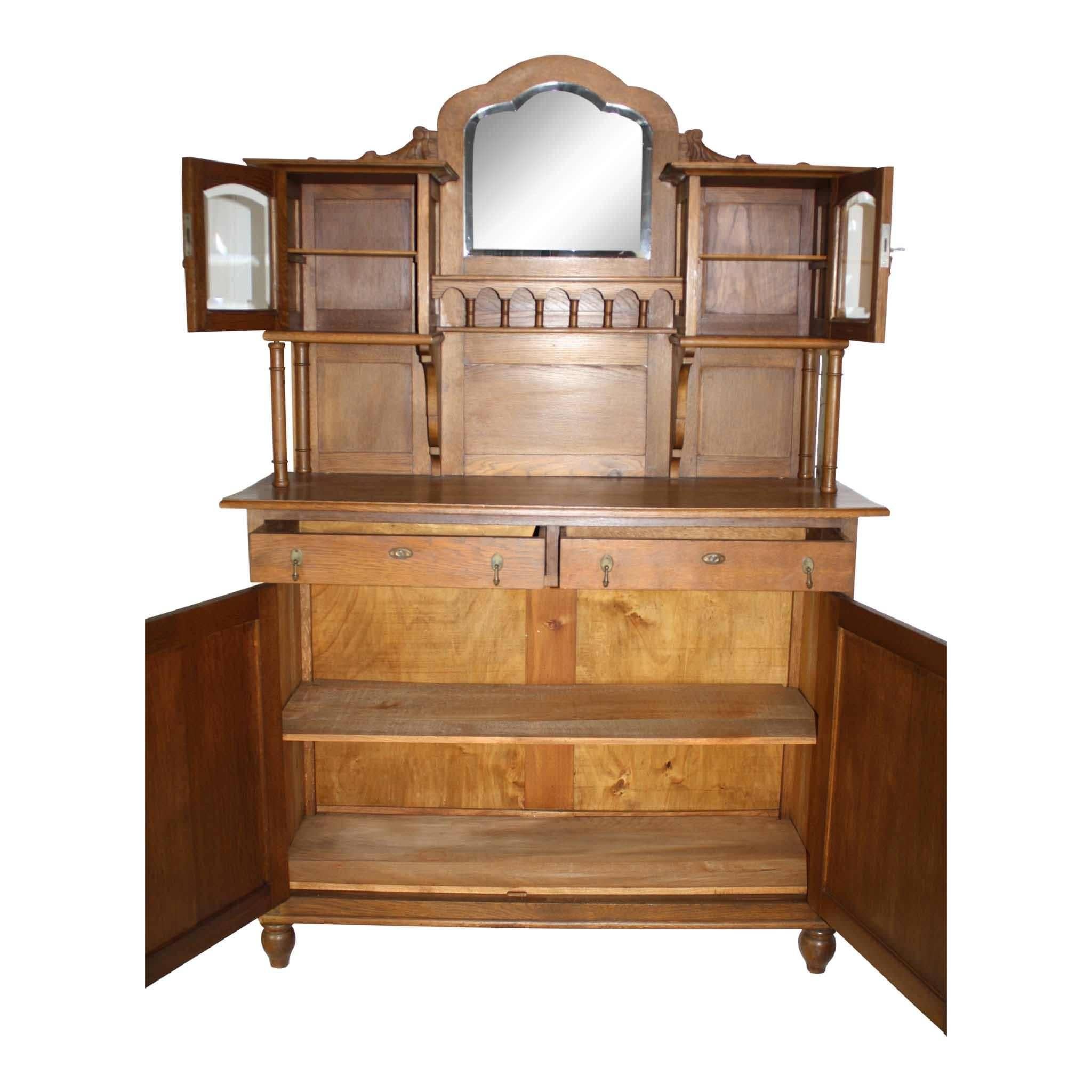 The upper gallery of this oak buffet consists of a beveled mirror with two-glass doors on either side. The gallery is supported by candlestick risers and decorative brackets. The lower portion of the buffet is comprised of two drawers above double