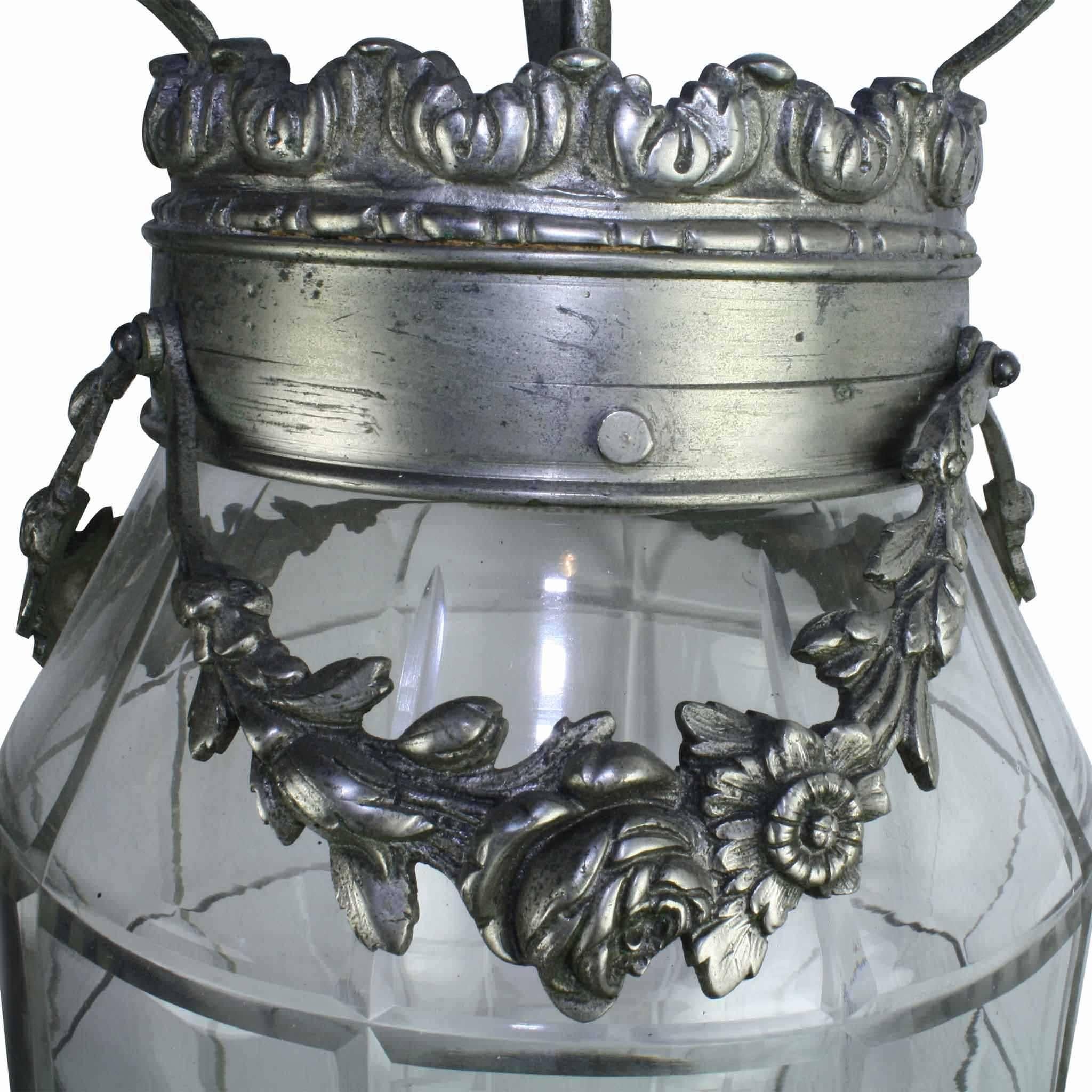 Spanning the Art Deco and Art Nouveau stylistic periods, this lantern features a floral vine that falls in graceful lines about the top crown. The lantern has a decorative canopy and chain. An ornament finial of a bunch of grapes caps the bottom.