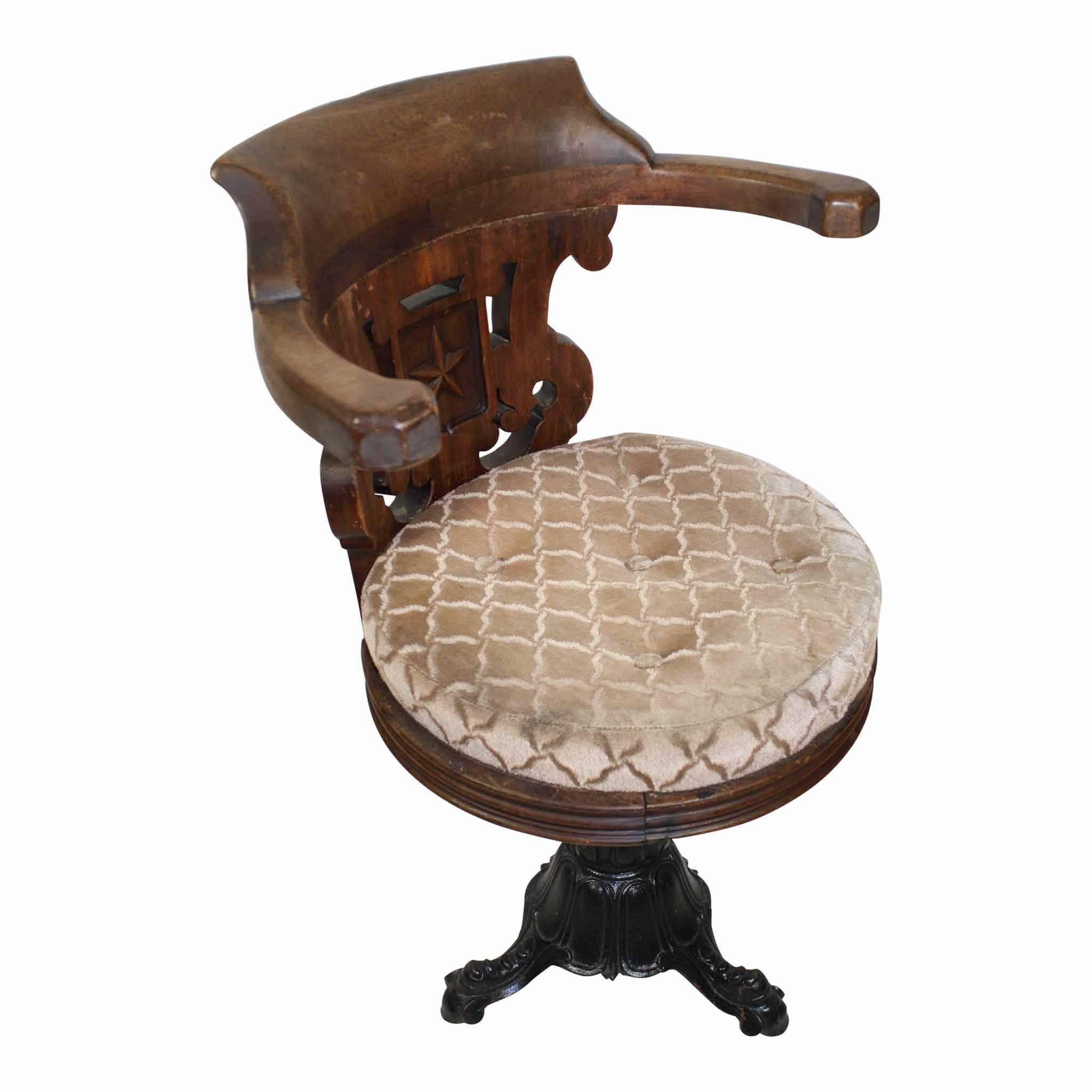 This "captains" style chair has curved, horizontal, raised arms supported only by the back. The chair back has a pierced design with a five point star carved at the centre. The tufted, round seat is upholstered with a light beige fabric.