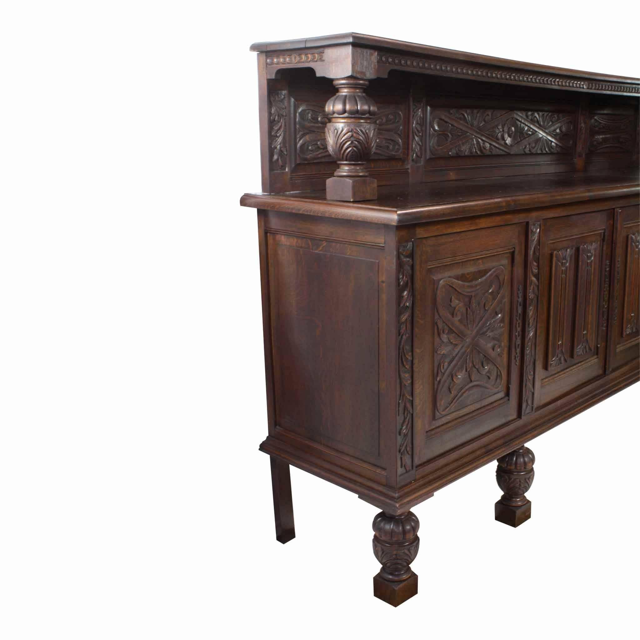 The center doors are reeded and capped at the top and bottom with foliage. The outer doors are carved with a geometric pattern of foliage, which matches the carvings on the backboard. Acorn style legs and risers give the sideboard height. The top