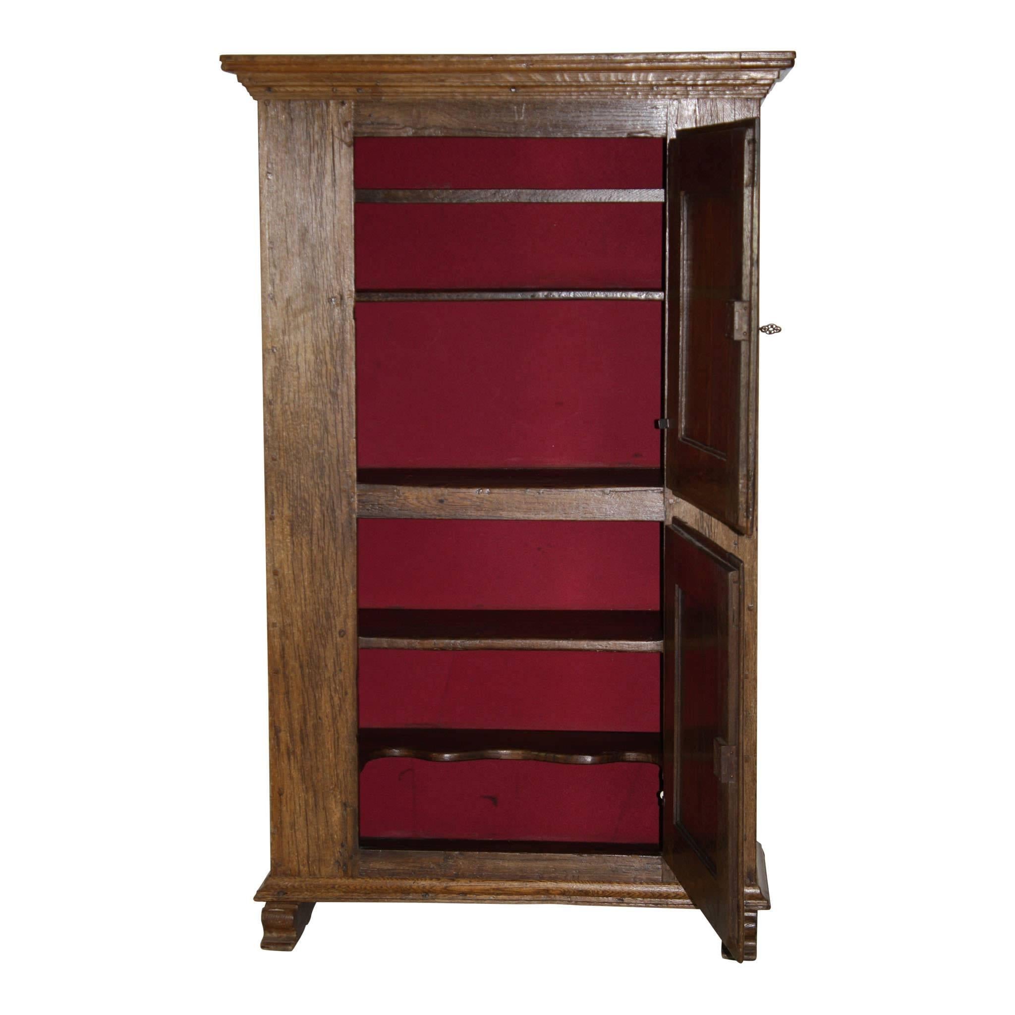 The solid construction of this red oak cabinet makes it a weighty piece. It has five shelves behind two doors, the lower shelf has three recesses. The doors have carvings of small shells at each corner. Its back interior has been covered in red