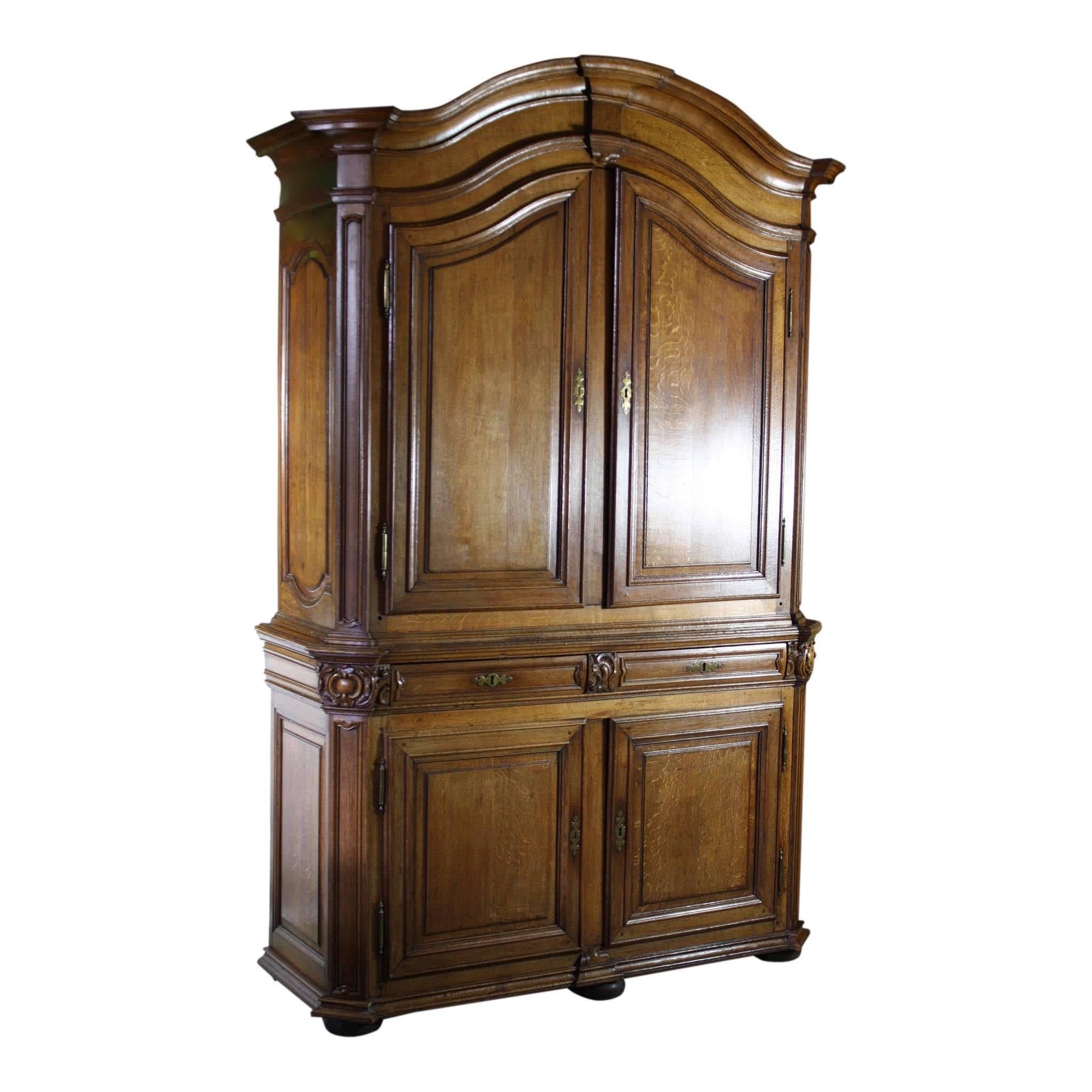 This spacious double bodied cabinet has a gracefully arched crown, two center drawers, brass escutcheons, hinges, iron interior door locks and bun feet. The upper portion has two scalloped shelves. Height of lower portion is 41 inches. No key.