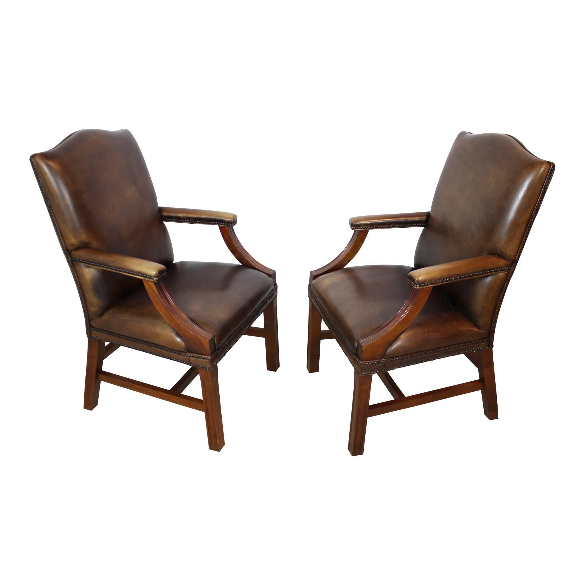 Two, dark brown, arched back leather chairs are coupled with generous, deep seats and padded leather armrests. The sturdy, well cared for leather, is secured with brass pinning and has a beautiful patina from years of use.