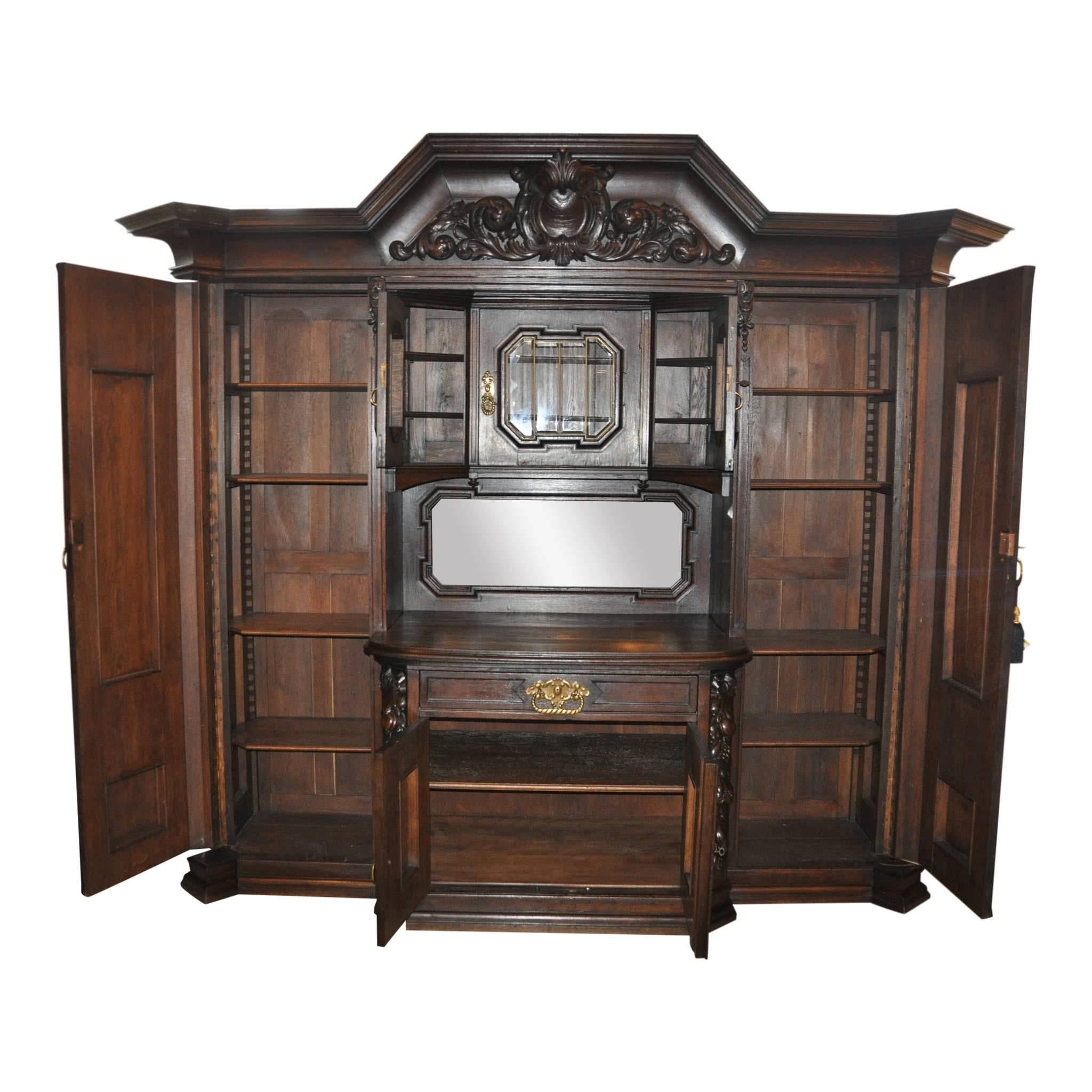 On offer is a large oak wall unit from Danzig Germany. Two large side doors open to reveal four adjustable shelves each. More storage in the upper cabinet surround, with three glass doors and two shelves. The lower case is comprised of a drawer and