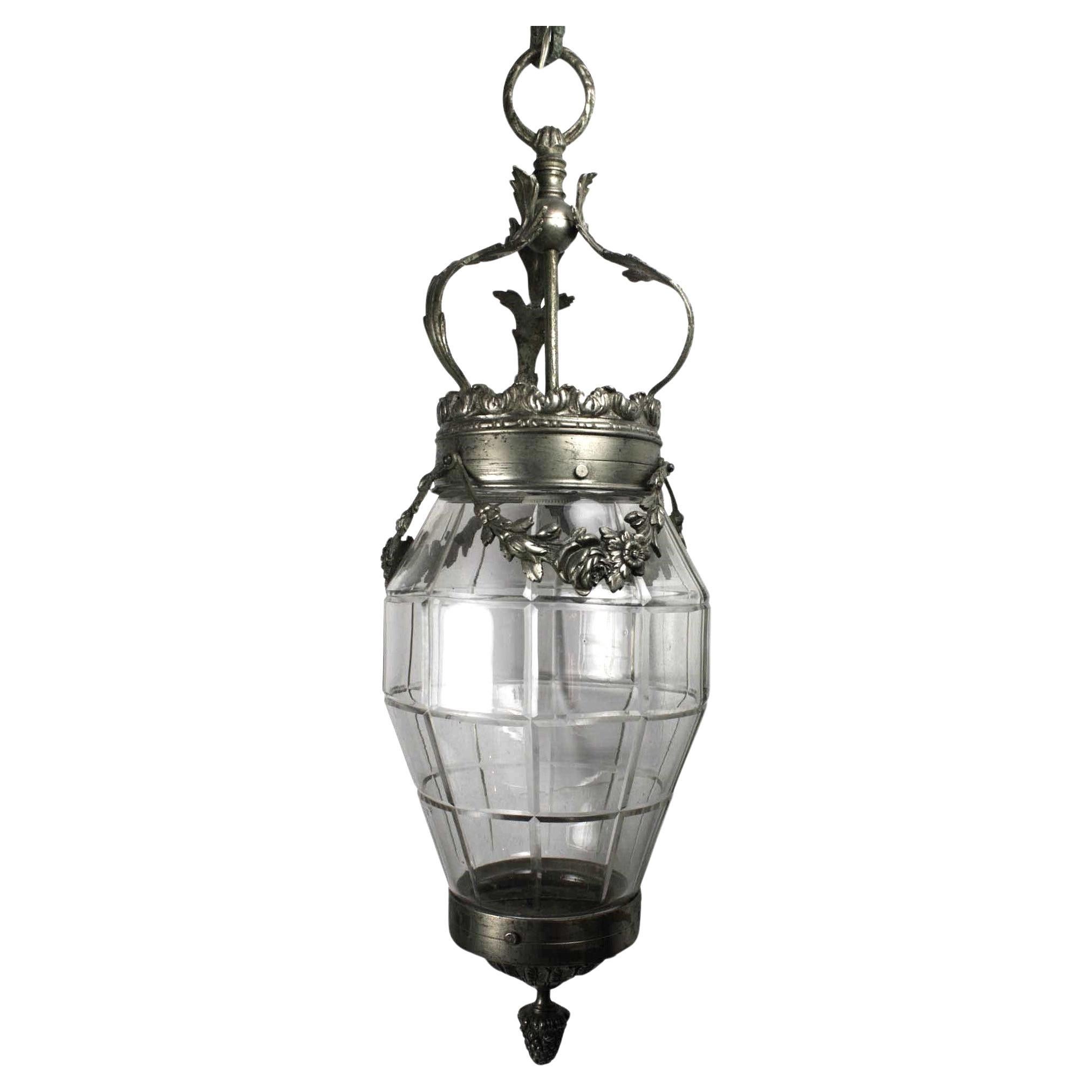 Abarcando los periodos estilísticos Art Déco y Art Nouveau, este farol presenta una enredadera floral que cae en elegantes líneas sobre la corona superior. El farol tiene un tejadillo decorativo y una cadena. Un remate ornamental de un racimo de