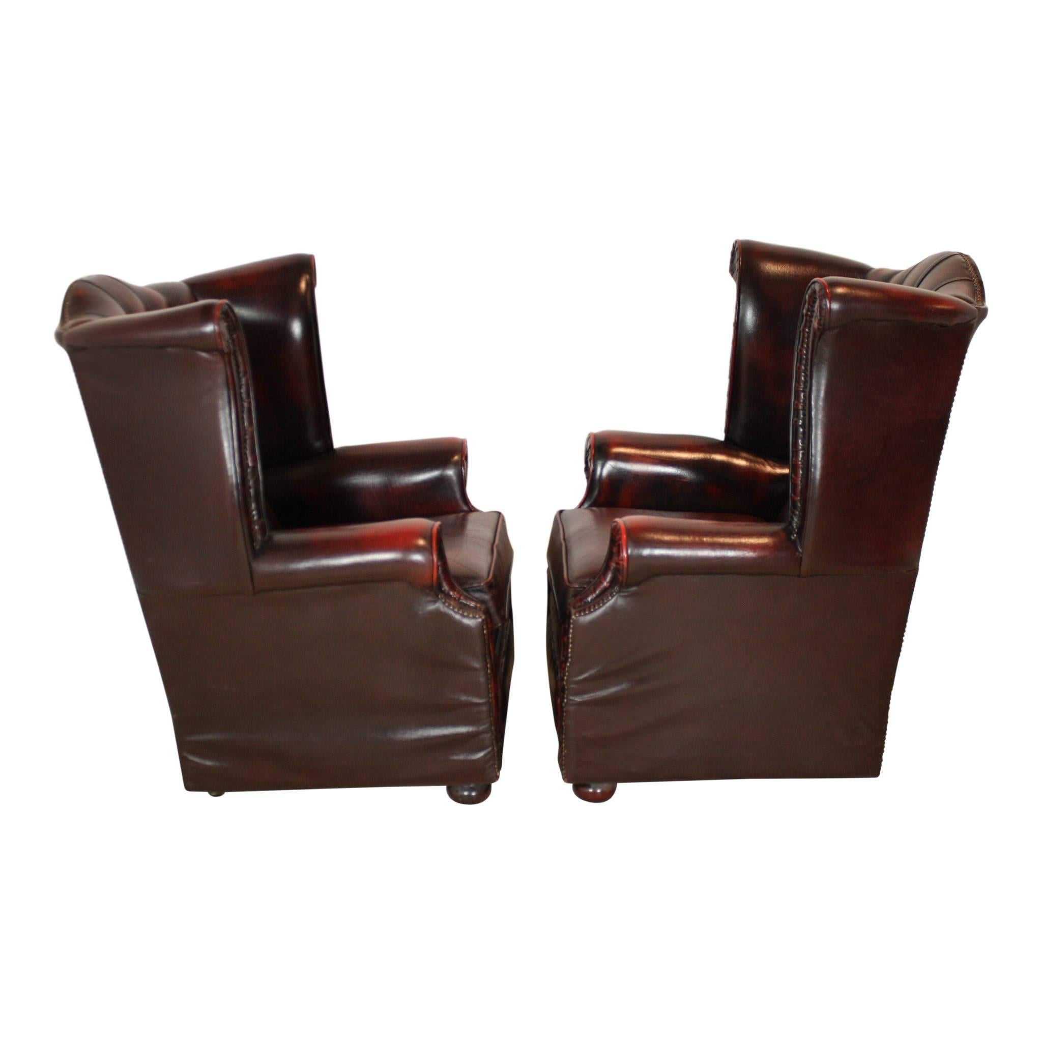 Upholstered in dark reddish-brown leather, this oxblood set of Chesterfield chairs is both handsome and distinguished. The leather is secured with silver studding along the front, back, top, and wing facings. The chairs backrests are tufted. Bun