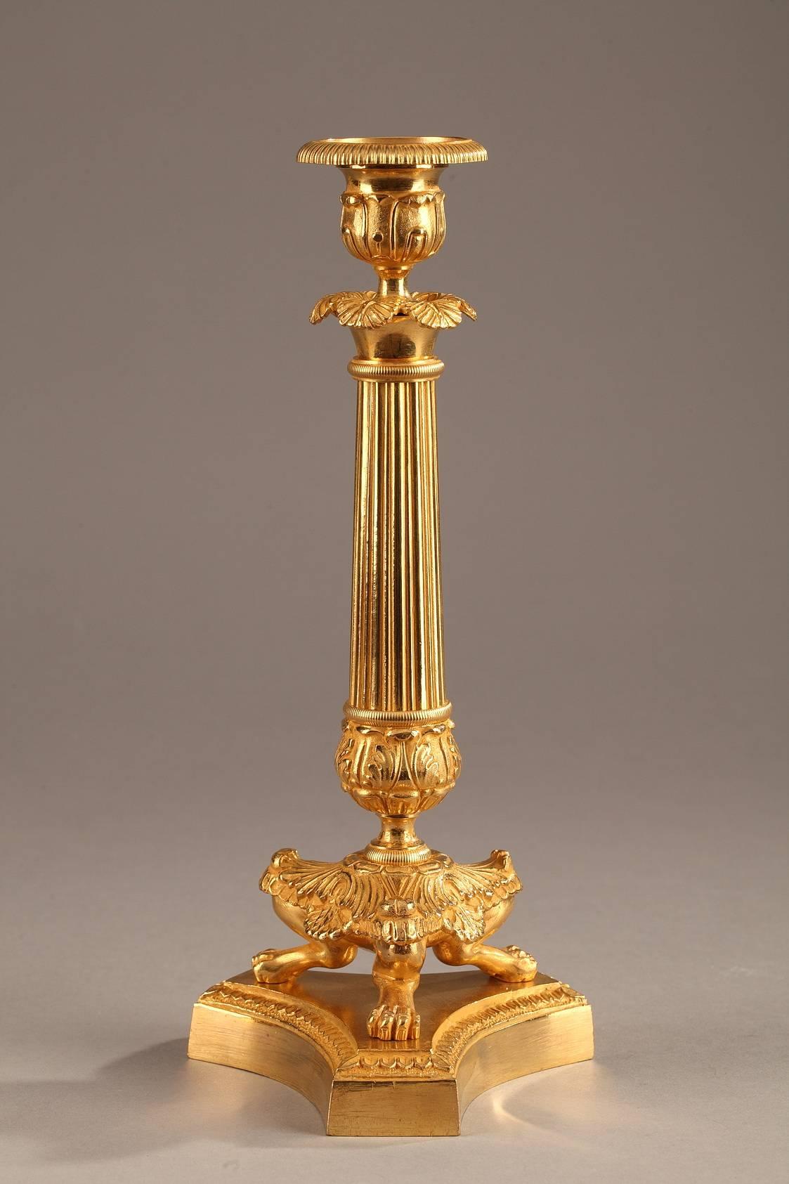 Pair of candlesticks in gilt bronze. They are in the shape of columns that rest on three clawed feet and are set on a three-pointed base. The fluted shafts of the candlesticks are intricately sculpted with acanthus leaves and palmette. Restauration