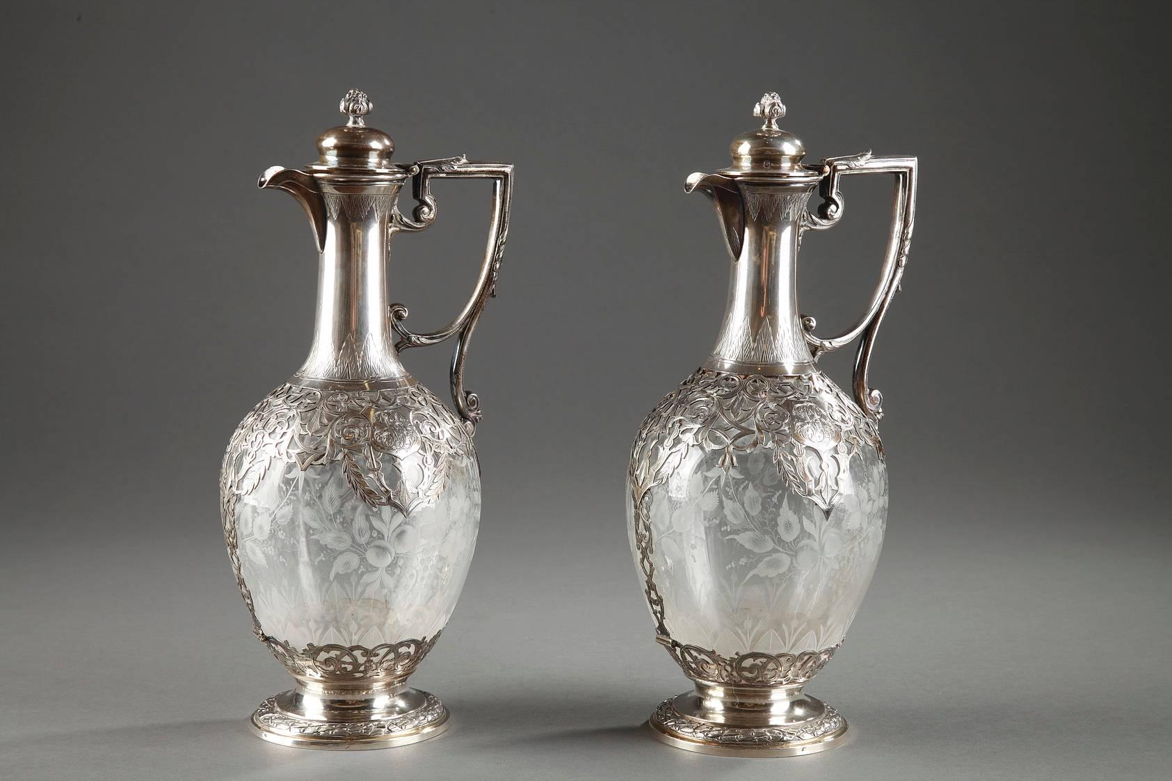 Pair of late 19th century crystal ewers framed with silver. Each crystal paunch is intricately engraved with flowers and leafy branches. The silver collar and base are richly decorated with openwork interlacing, varied foliage, and a monogram. The