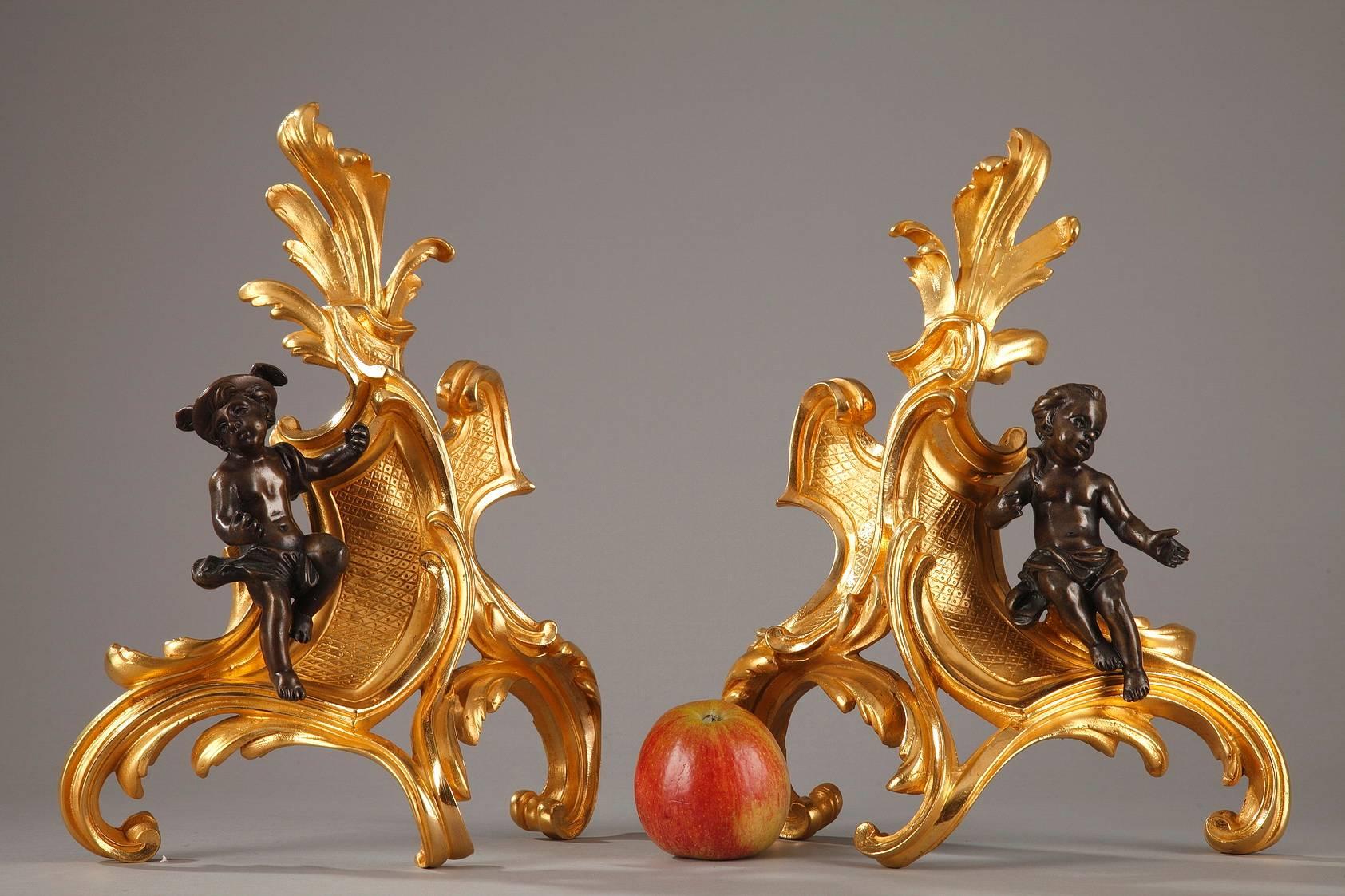 Pair of gilt and patinated bronze andirons decorated with Hermes and Herse. Both figures are represented as children with Hermes (Mercury in Roman mythology) wearing his winged hat looking away from Herse (the daughter of the Athenian king Cecrops),