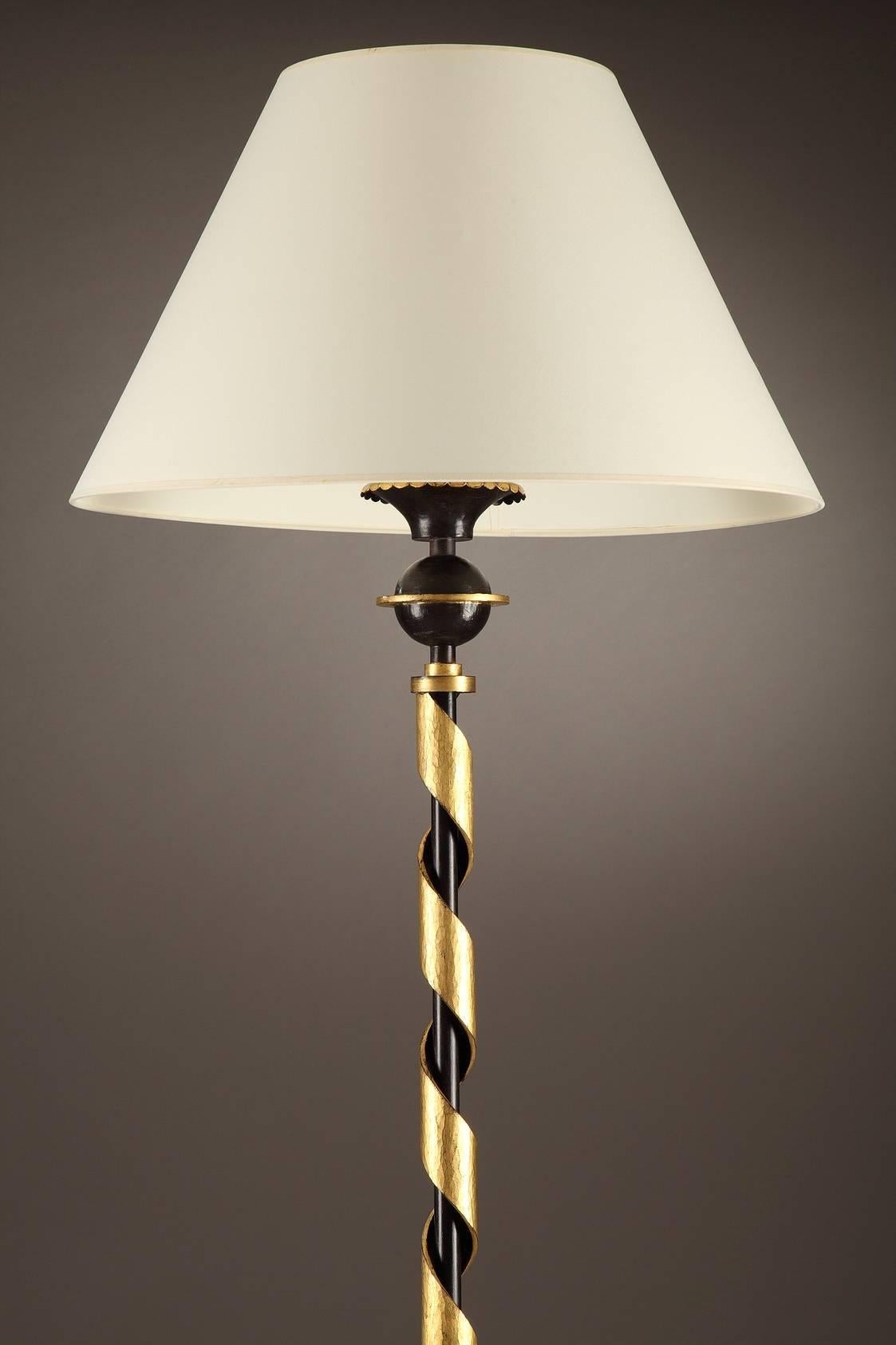 Floor lamp by Gilbert Poillerat featuring patinated and gilt wrought iron. The patinated cylindrical center shaft is embellished with a gilded spiraling band that is topped with a sphere bisected with a disk. It rests on a base with four coiled and