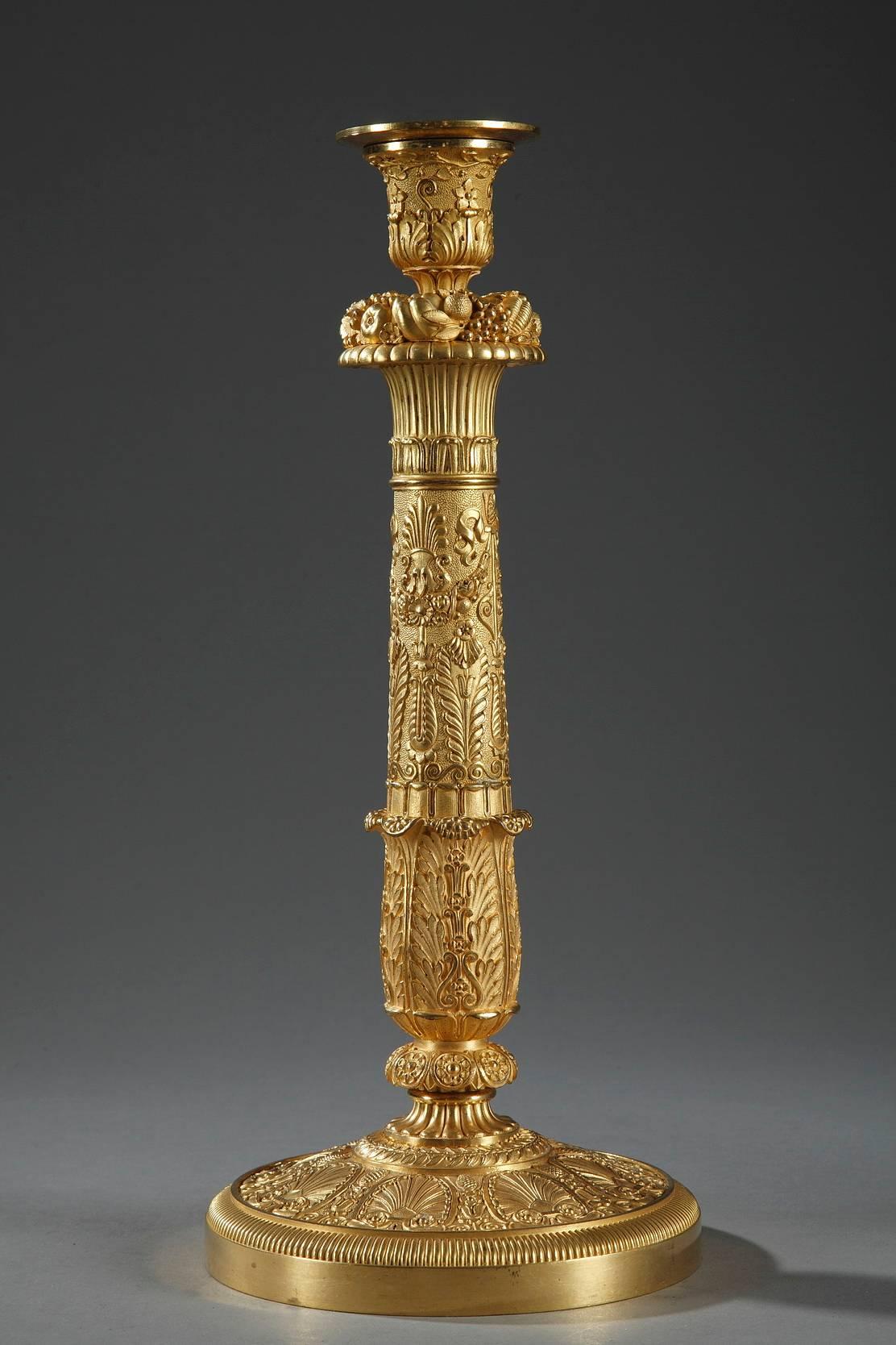 Pair of candlesticks from the Charles X period in gilt and sculpted bronze. They are richly ornamented in palmettes, ivy, and small flowers on a matte background. The barrels are topped with a ring of flowers. Each candlestick rests on a circular