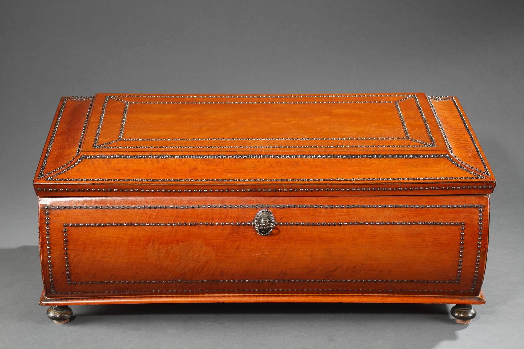 Rectangular box for storing shawls in wood burr veneer. Light ebony stripes and small beads underline the elegant forms of the body and lid. The handles and toupie feet are in iron. The interior is lined with off-white silk, and inside of the lid is